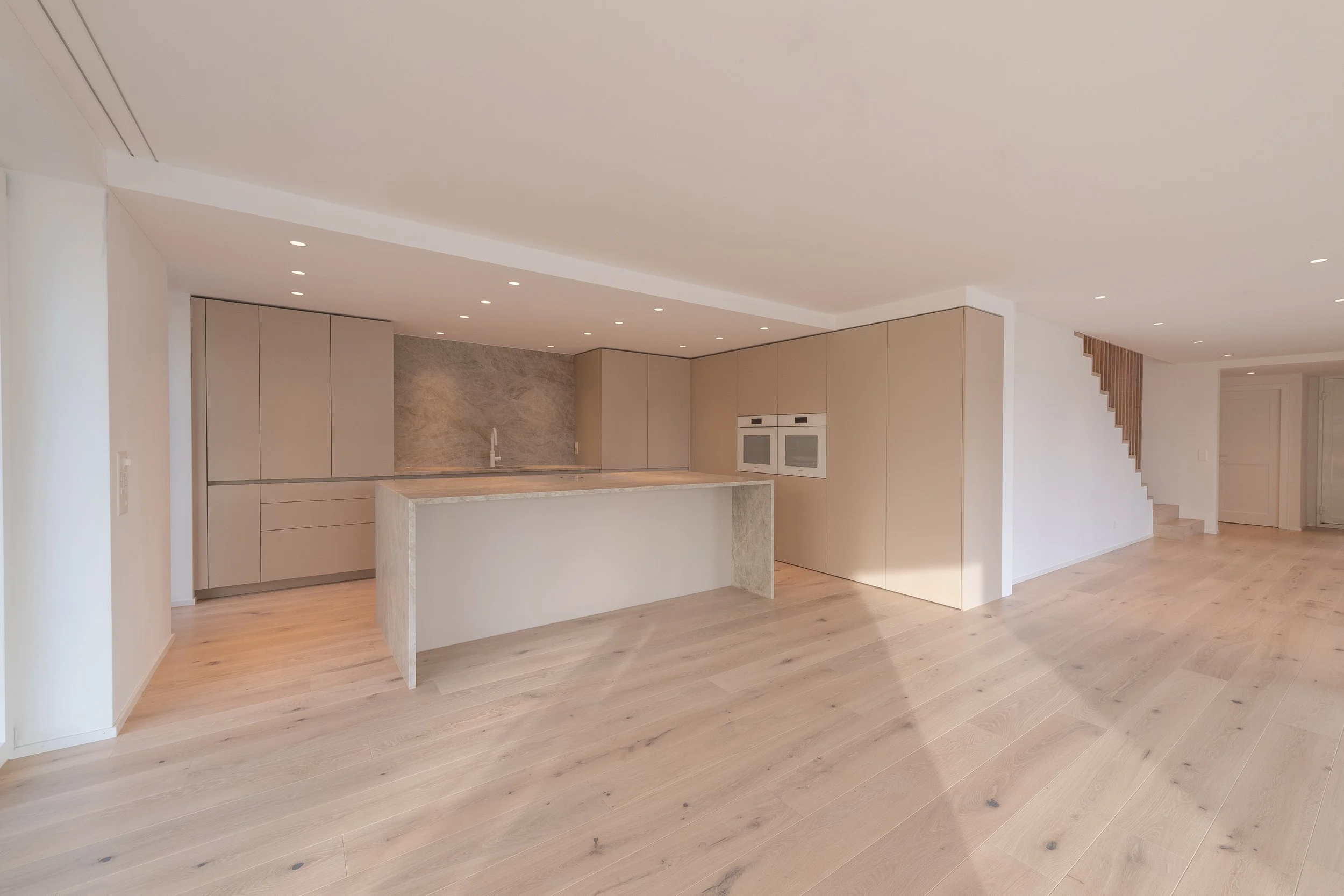Moderne, offene Küche mit beige Schränken und einem Kücheninsel in einem hellen, minimalistischen Wohnraum.