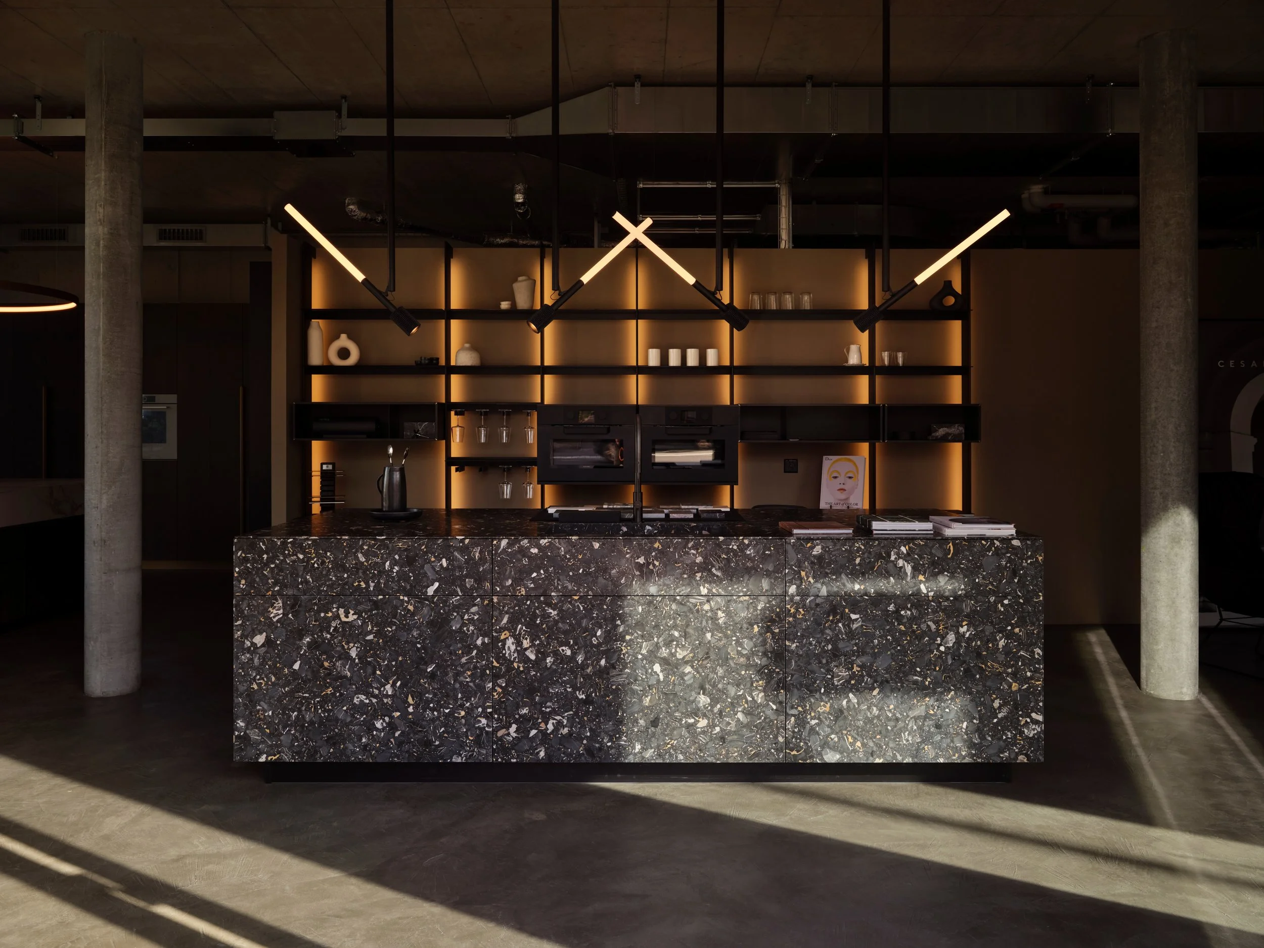 Moderne Hotelrezeption mit dunklem Marmor-Schreibtisch, schwarzer Wandregale mit Dekorartikeln und stilvollen Leuchten.