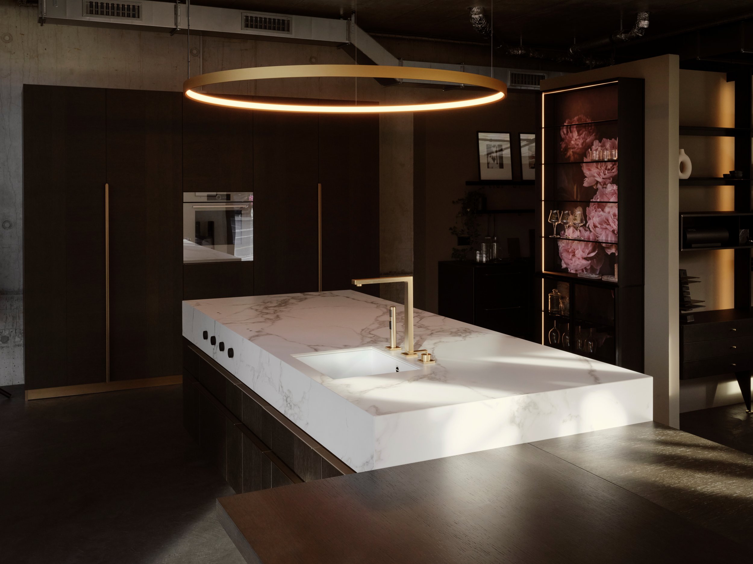 Moderne Kücheneinrichtung mit weißem Marmorkochinsel, schwarzen Schränken, Goldarmaturen und dekorativen Elementen wie Bildern und Vasen, in einem industrial-style Raum mit sichtbaren Deckenleitungen.
