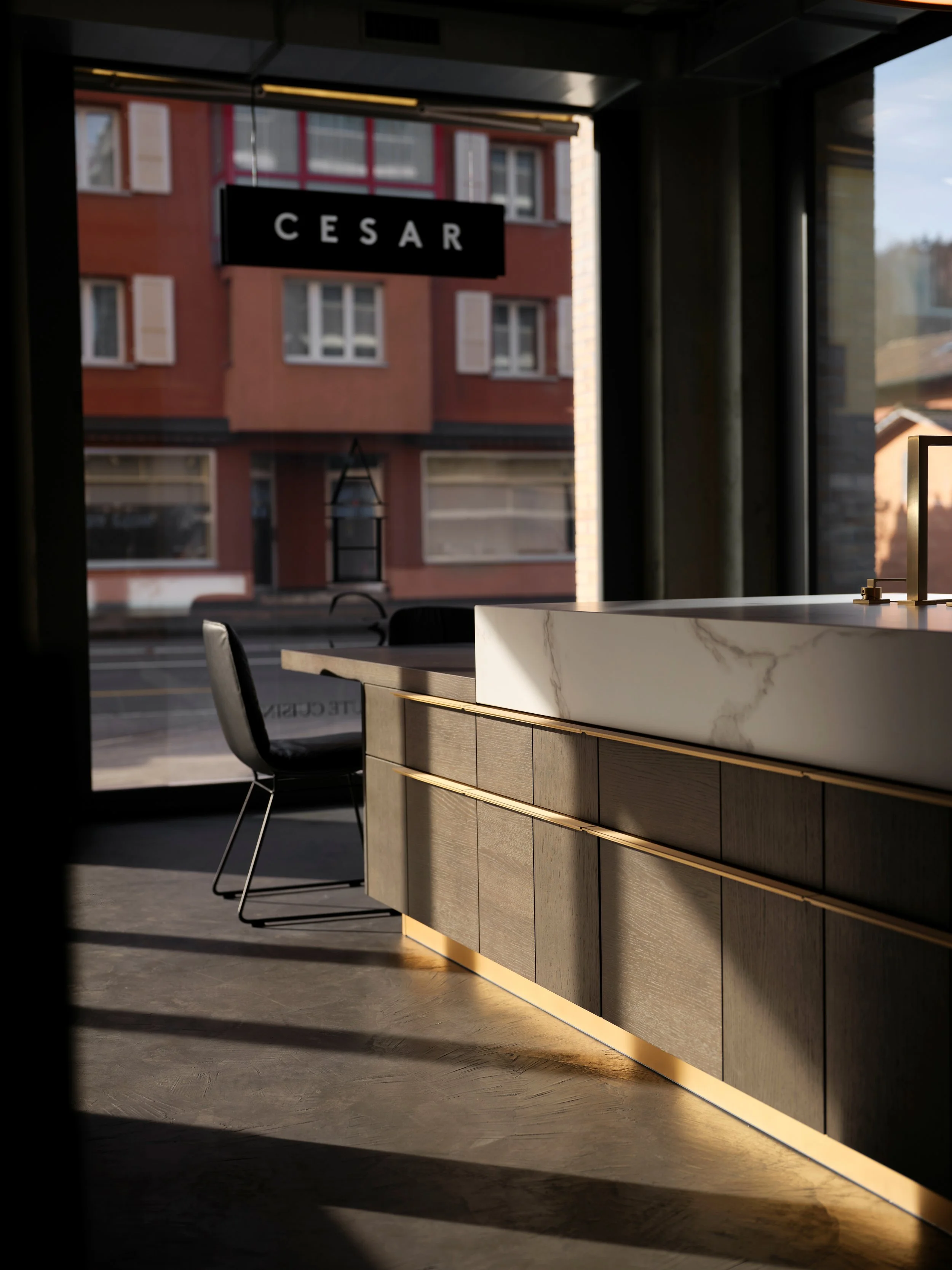 Innenansicht eines modernen Raumes mit einer langen Theke, schwarzes Stuhl, große Fenster, die Tageslicht hereinlassen, und eine Außenansicht eines Hauses mit roten und weißen Fenstern sichtbar.