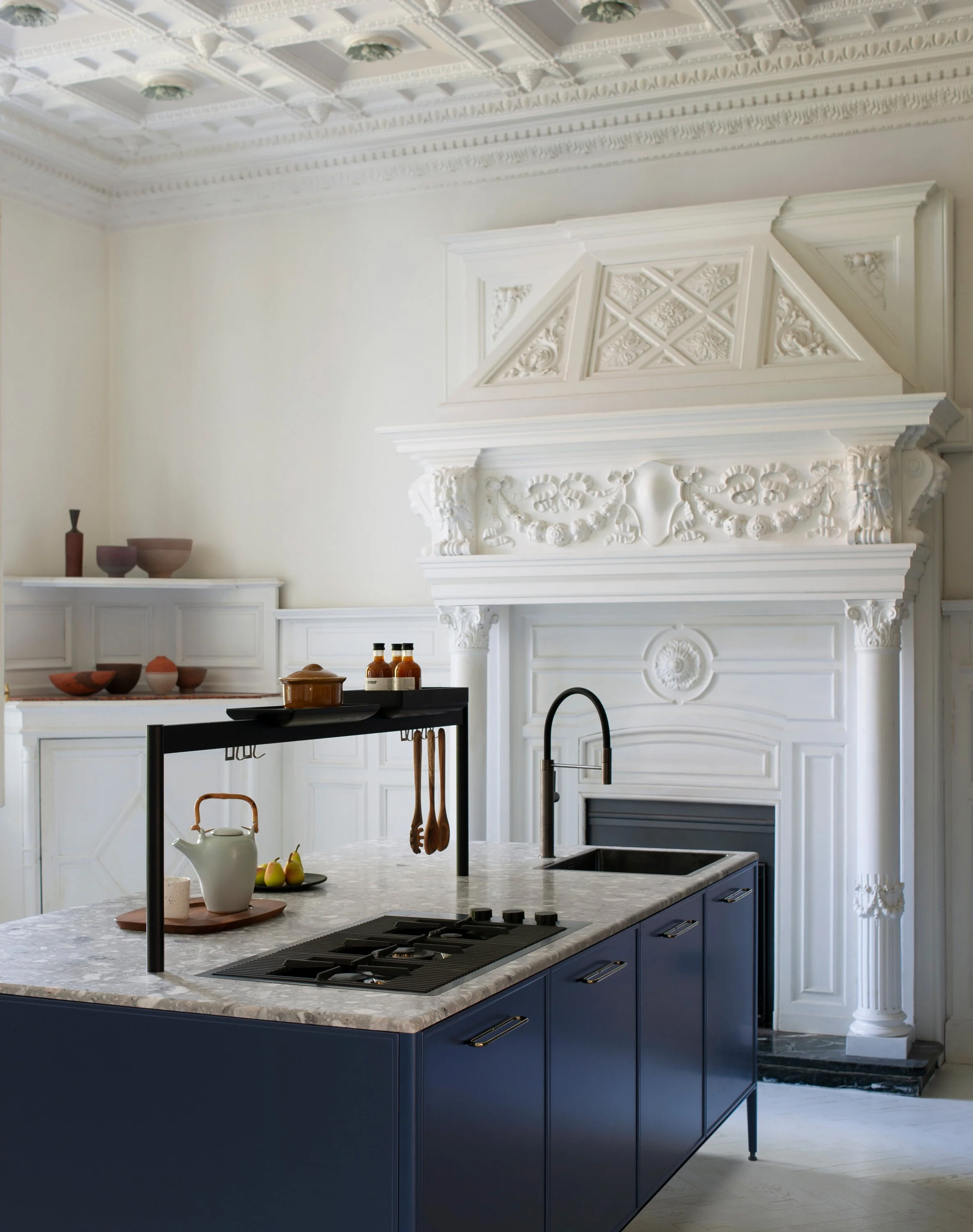 Eine moderne Kücheneinrichtung mit blauer Kücheninsel, weißen und dunklen Ablageflächen, und eleganten weißen Wand- und Deckenverzierungen.