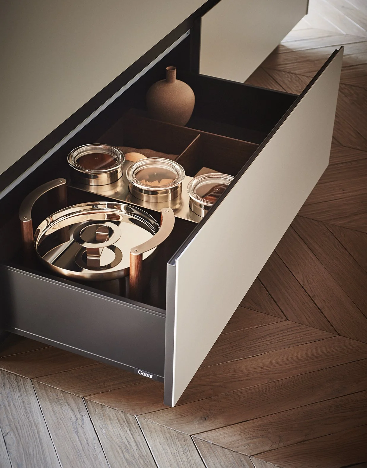 Ein moderner Herd mit Toaster-Design, geöffneten Schubladen und unterschiedlichen eingelagerten Küchenutensilien auf einem Holzboden.