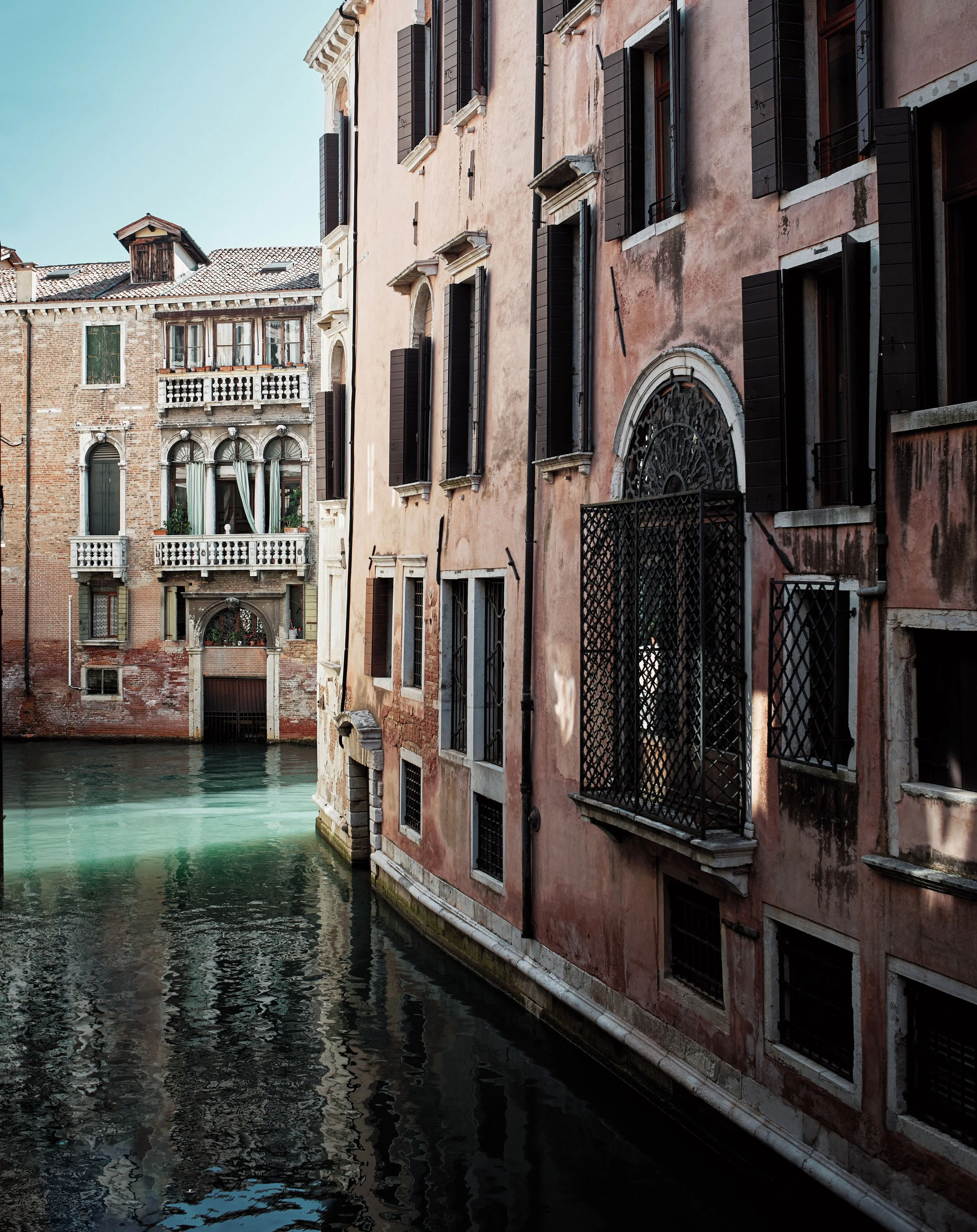 Aufnahme von einem Kanal mit angrenzenden alten, mehrstöckigen Gebäuden in Venedig, Italien, bei Sonnenuntergang.