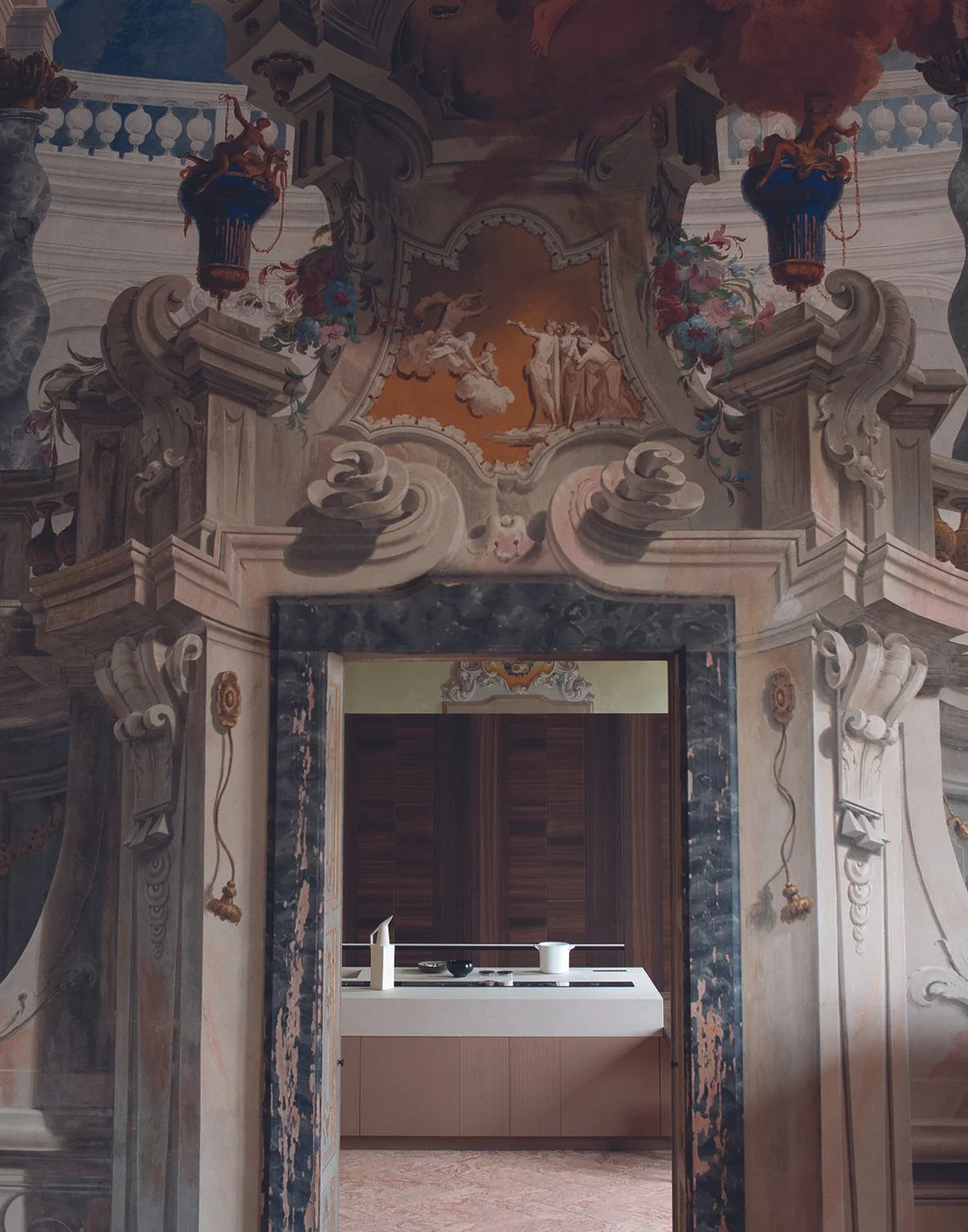 Barocke Decke mit Fresken und kunstvollen Verzierungen, Blick durch einen Türrahmen in eine moderne Küche.