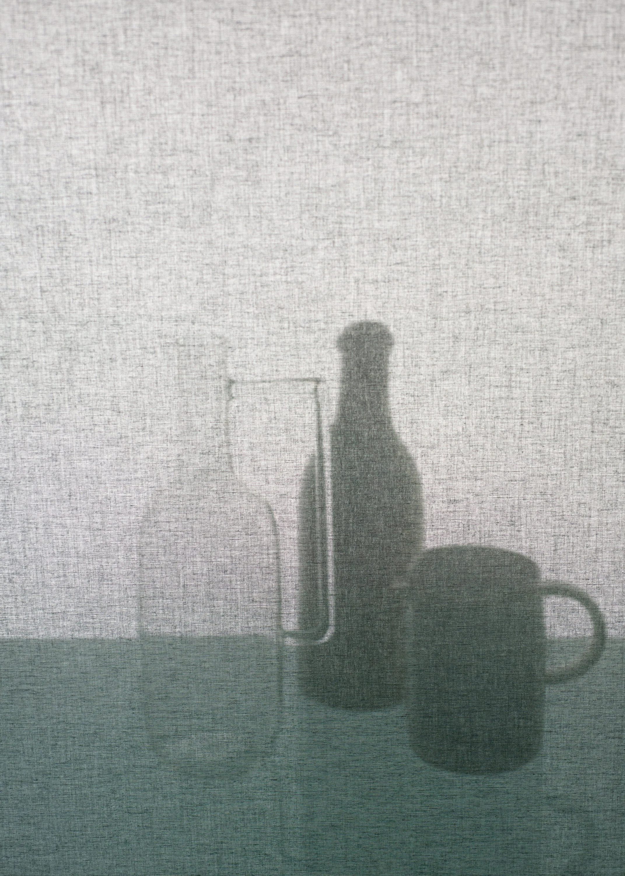 Ein unscharfes Bild eines gläsernen Behälters, möglicherweise eine Flasche, auf einer Tischfläche, mit einer Technologie- oder Geräteschatten im Hintergrund.
