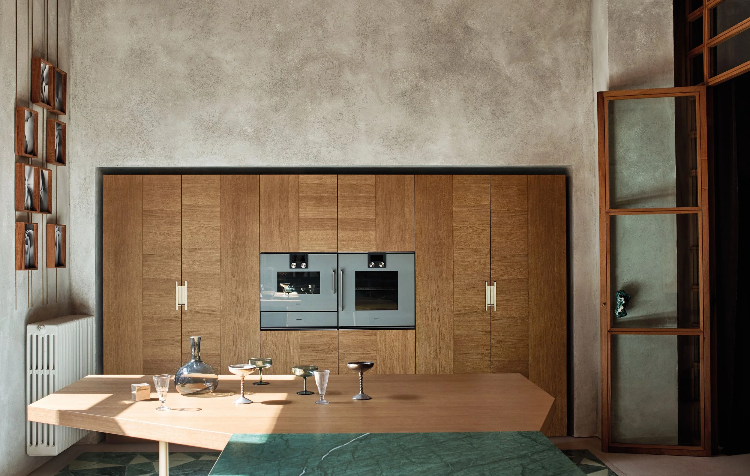 Moderner Küchenraum mit Holzmöbeln, einer grünen Marmortheke, dekorativen Gläsern auf einem Holztablett und Wanddekorationen aus Holz.