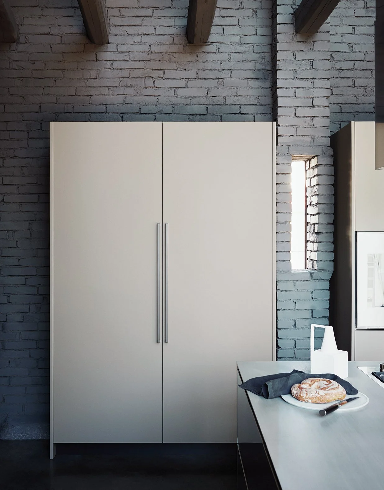 Eine moderne Küche mit weißen Schränken vor einer grauen Ziegelmauer, ein kleines Fenster auf der rechten Seite, eine weiße Vase auf dem Tisch, und auf dem Tisch liegt ein belegtes Brötchen mit einer schwarzen Serviette.