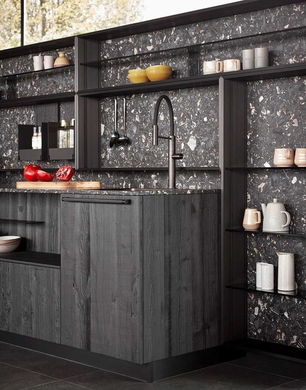 Moderne schwarze Küchenschränke mit dunklem Marmor-Backsplash, offene Regale mit Geschirr, Spüle und Wasserhahn, auf der Arbeitsplatte liegen rote Früchte.