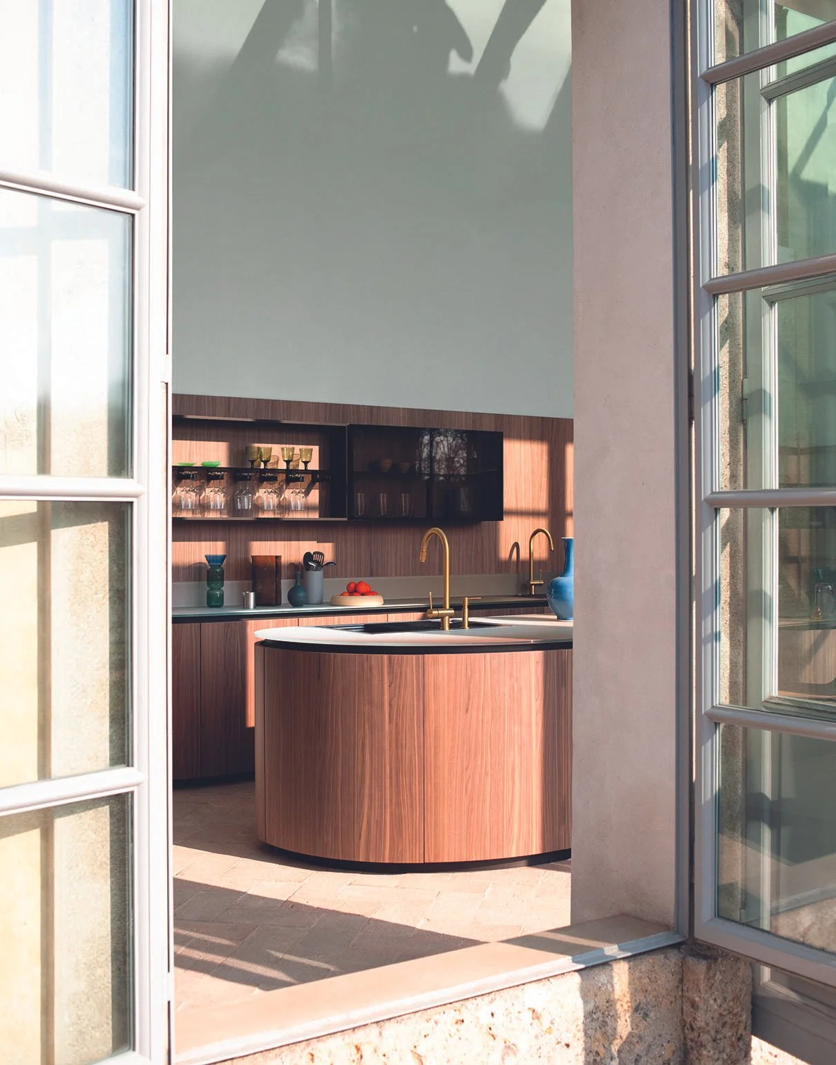 Moderne Küche mit Holzregalen, goldenen Wasserhähnen, blauer Vase und Obst, sichtbar durch eine offene Fenster-Tür