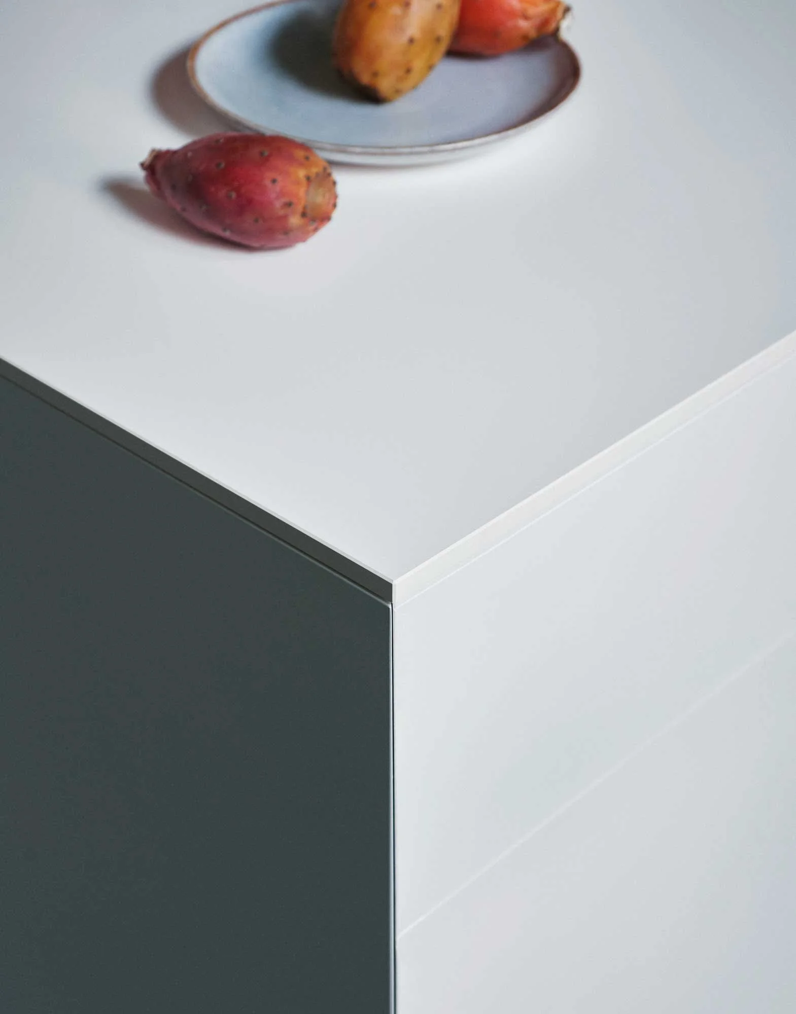 Drei rotes und ein braunes Ei liegen auf einem weißen Tisch, mit einem weißen Teller im Hintergrund, der mehr Eier enthält.