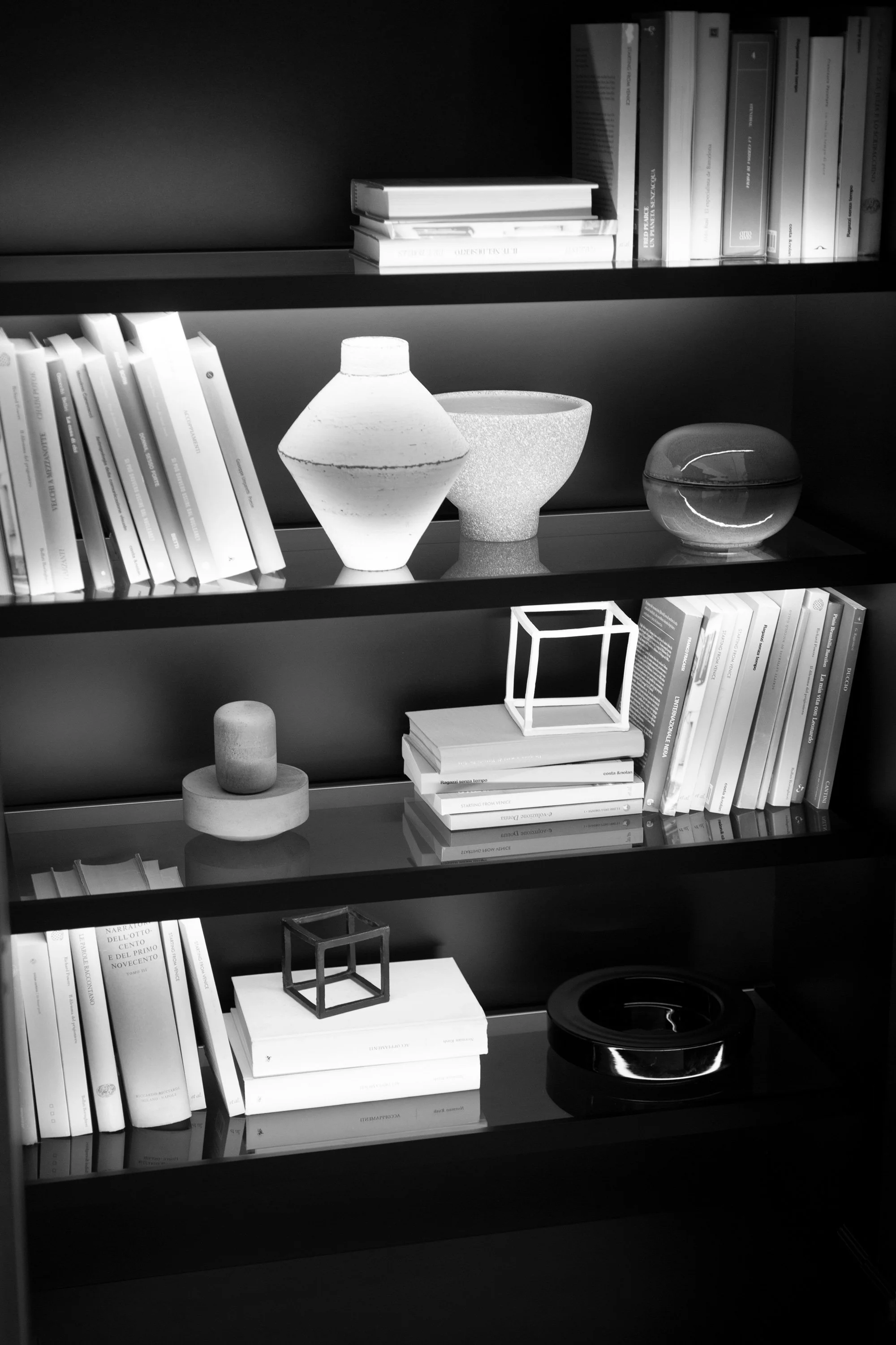 Schwarzer Bücherschrank mit weißen Büchern, dekorativen Vasen, geometrischem Deko-Objekt und einer schwarzen Schale.