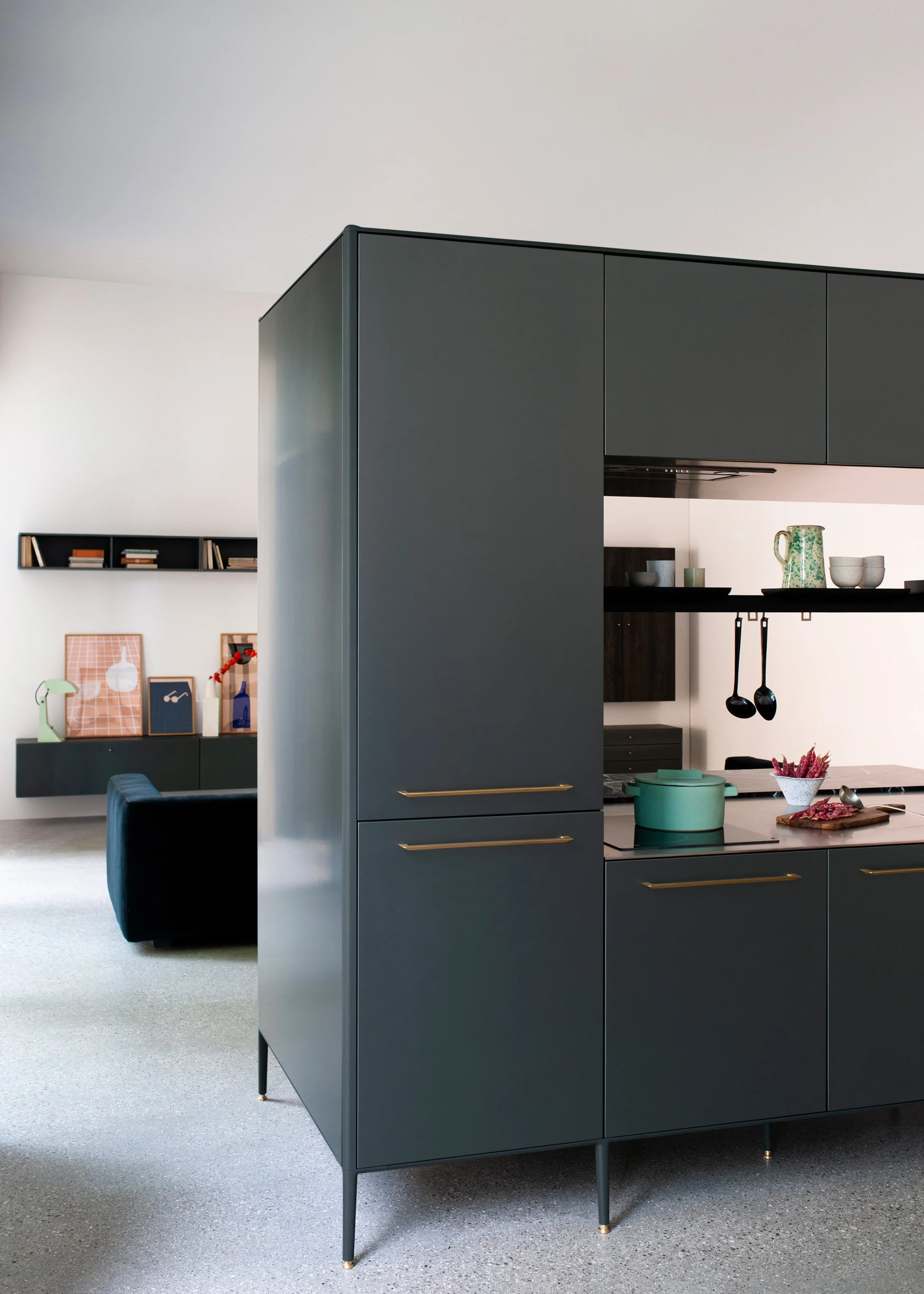 Moderner schwarzer Küchenblock mit eleganten goldenen Griffen in einer stilvollen offenen Wohnküche. Die dekorativen Regale mit Büchern und Wohnaccessoires sowie der graue Teppichboden schaffen ein luxuriöses und modernes Küchendesign mit hochwertige