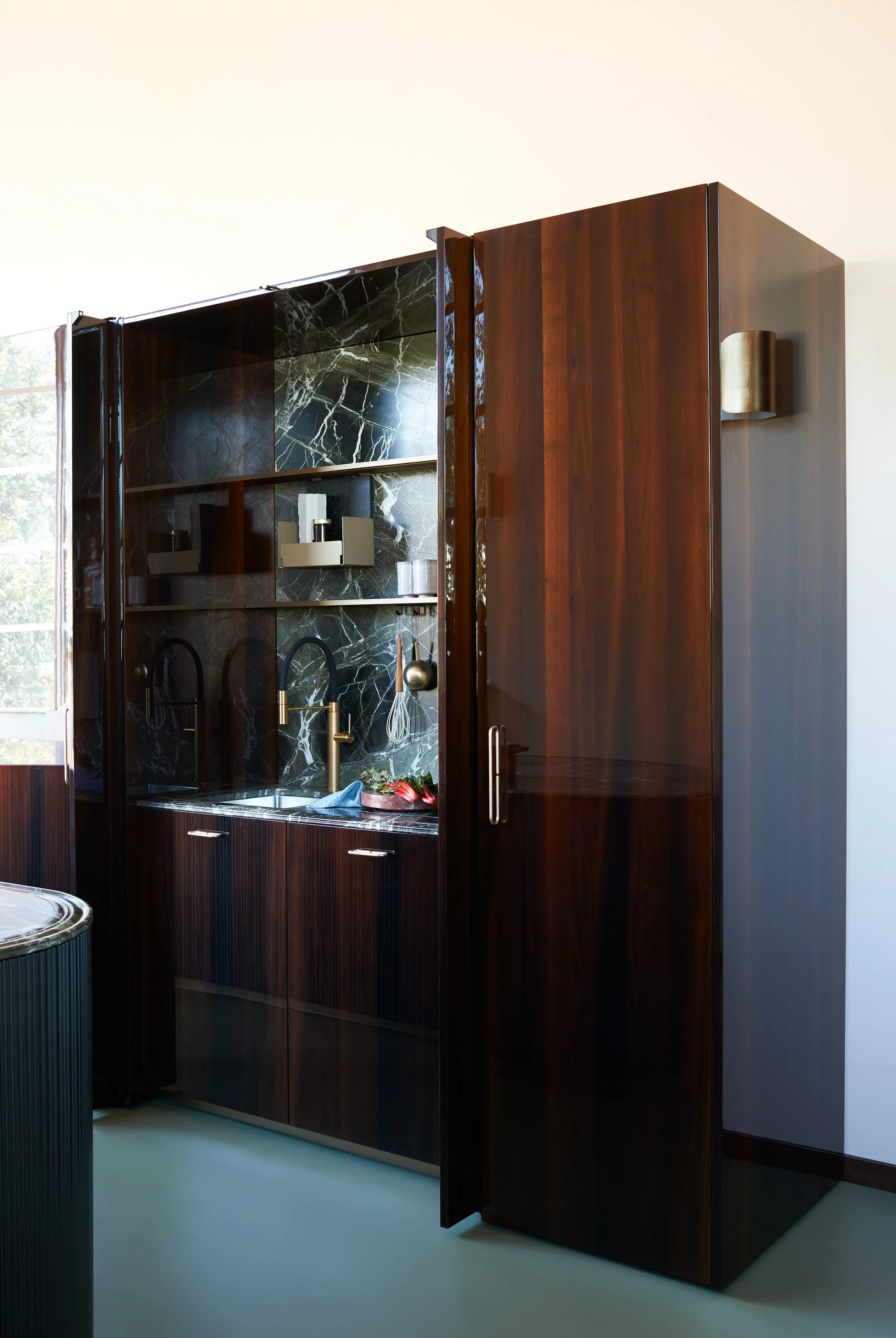 Ein moderner, dunkler Holzschrank mit glänzenden schwarzen Marmorabschlüssen im Küchenbereich.