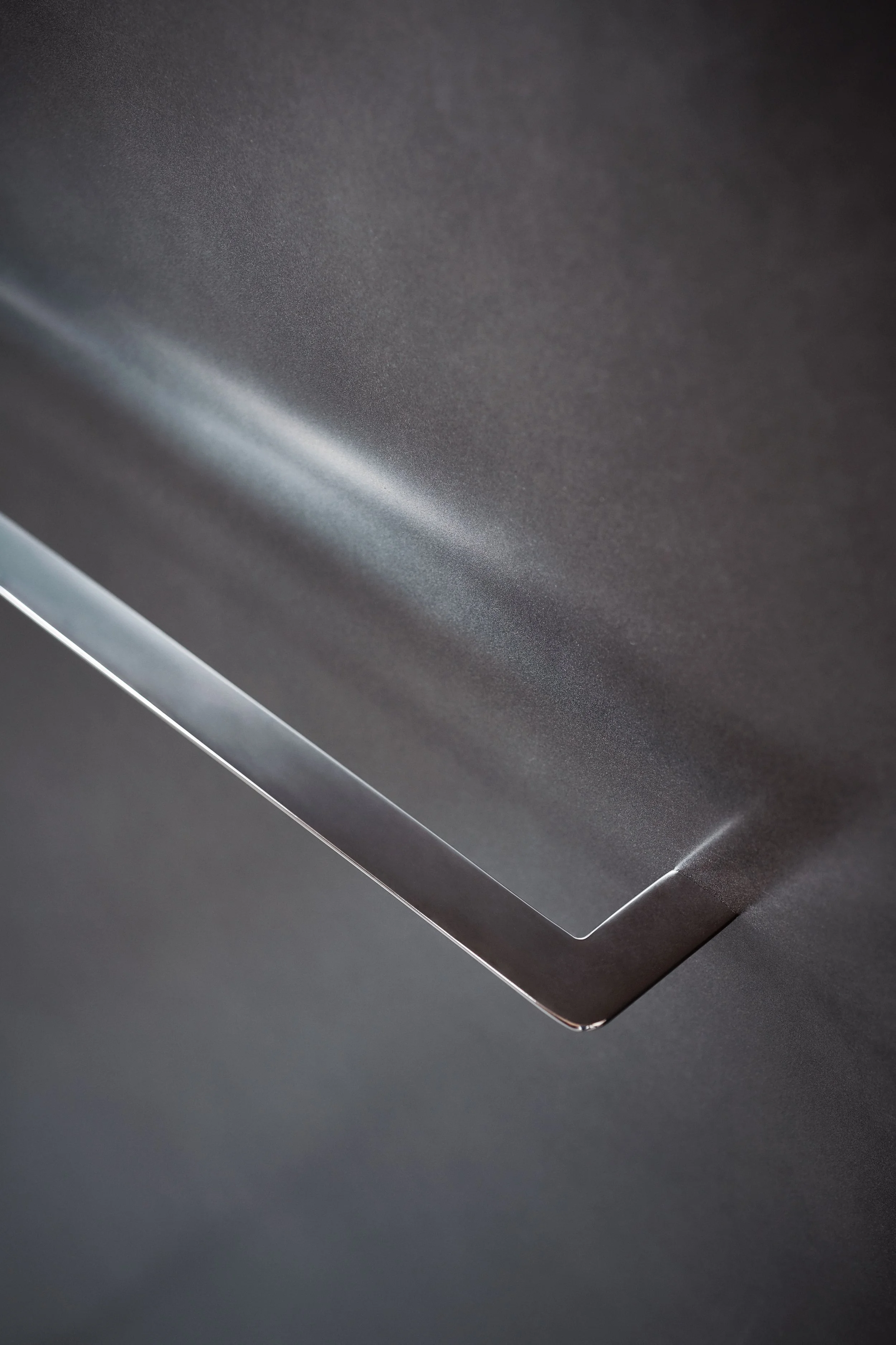 Nahaufnahme einer Metallfläche mit glatter, matter Textur, flexible Linienführung und schattierten Bereichen, auf einem dunklen Hintergrund.