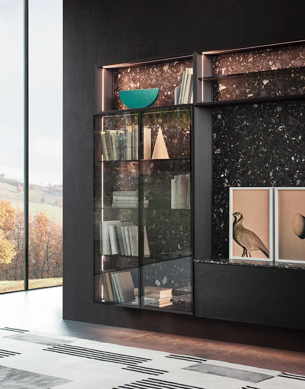 Ein moderner optisch ansprechender Bücherschrank mit Glastüren und schwarzem Marmor-Hintergrund in einem stilvollen Raum, neben großen Fenstern mit Blick auf eine Herbstlandschaft.