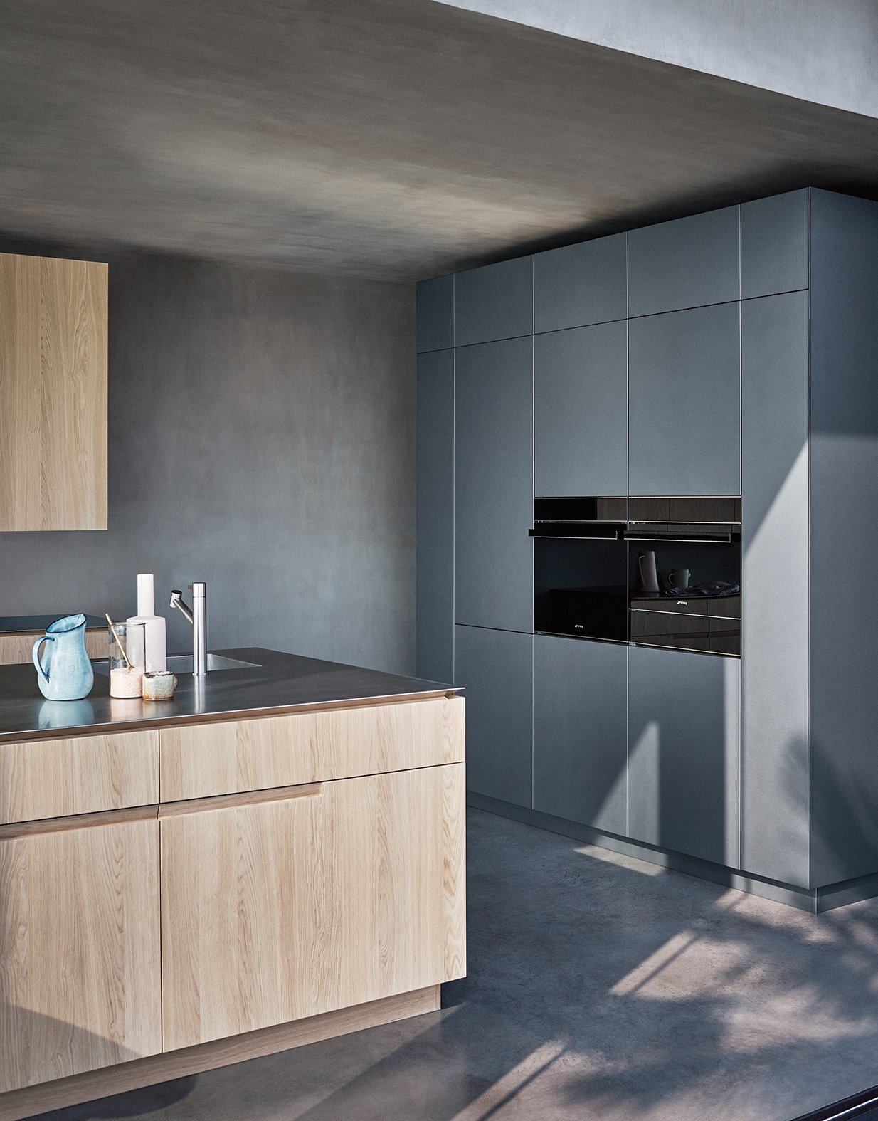 Moderne Küche mit Holz- und blauen Schränken, minimalistischer Stil, einige Küchenutensilien auf der Arbeitsplatte, Betonboden.