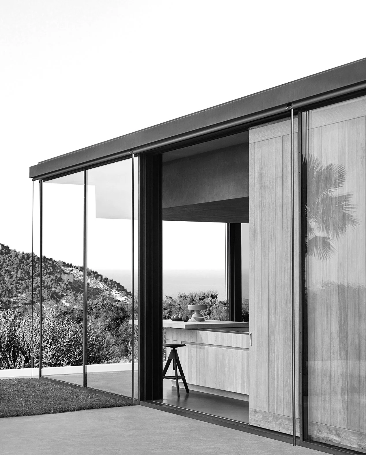 Modernes Haus mit großen Glasfassaden und Blick auf die Landschaft im Hintergrund, inklusive Palmenreflexion im Fenster