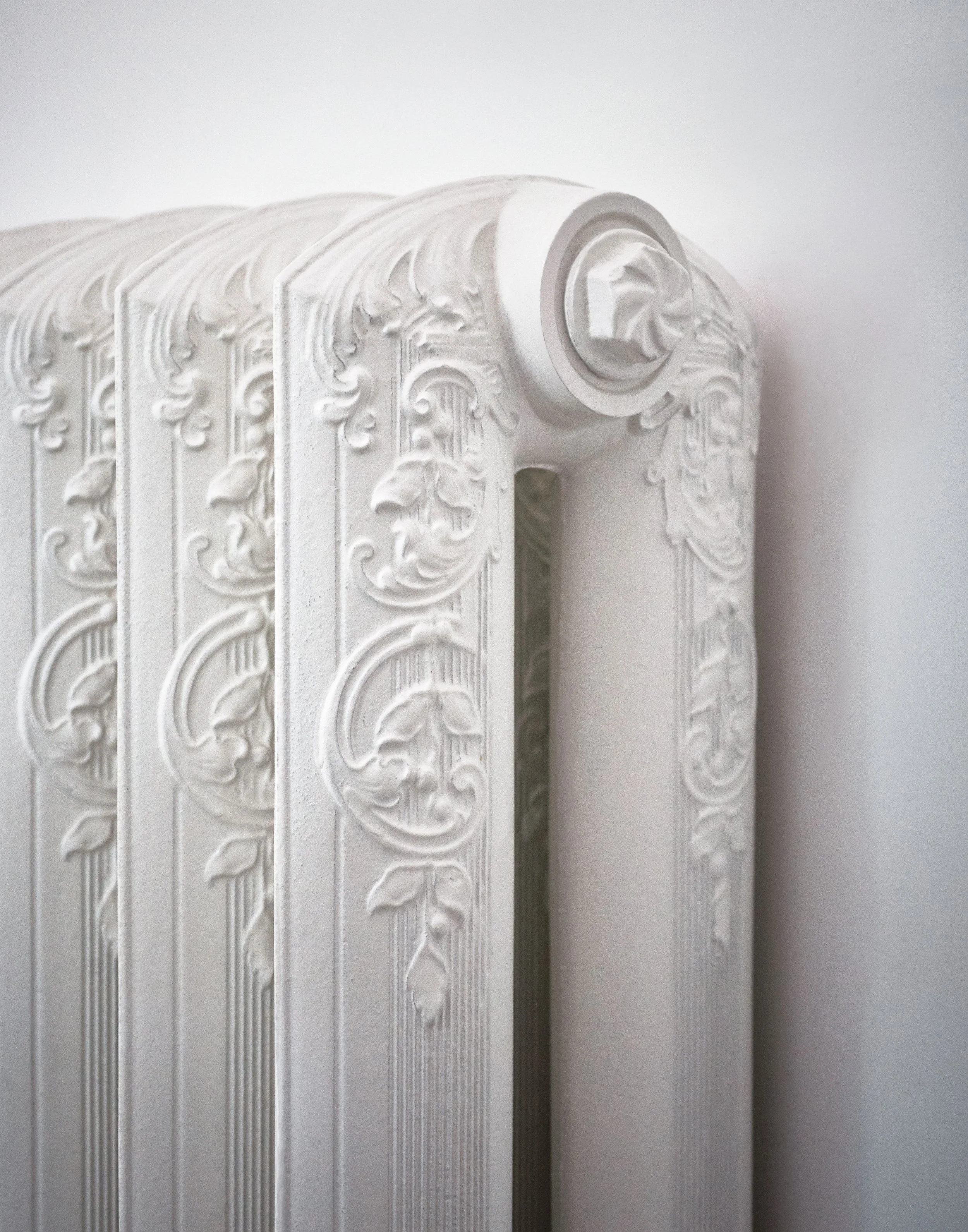 Ein weißer Heizkörper mit dekorativen ornamentalen Verzierungsmustern an rosettenartigen Enden, angebracht an einer weißen Wand.