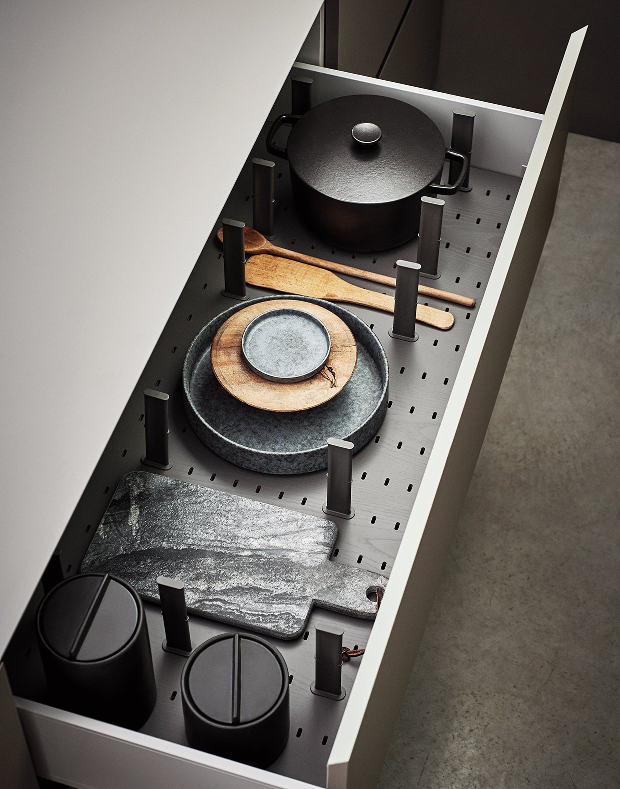 Ein schräger Blick in eine moderne Küchenzeile mit offenem Stauraum, darin eine schwarze Kochtopf, Holzlöffel, Schale, Platte, zwei schwarze Behälter und kochplatten.