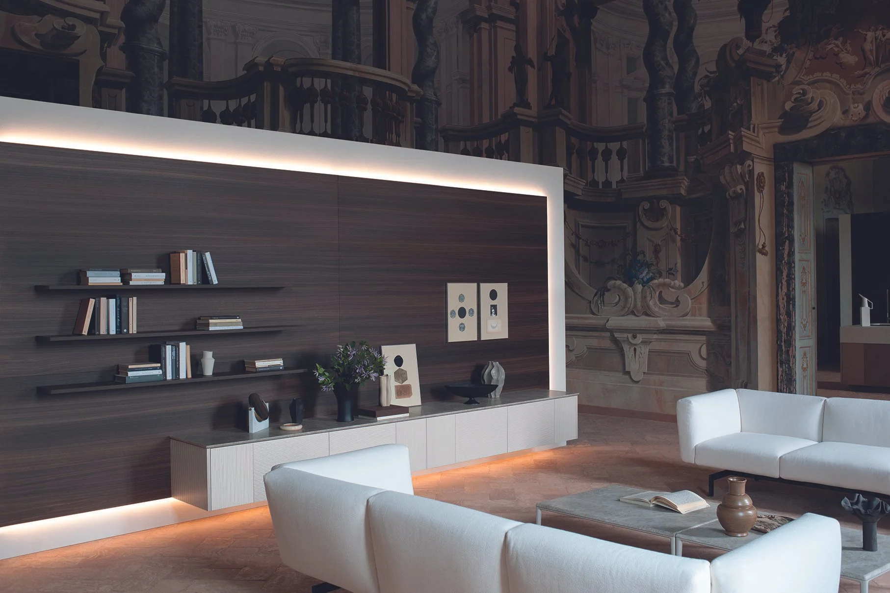 Moderner Wohnzimmer mit weißen Sofas, einer Holzvertäfelung an der Wand, dekorativen Wandbildern und dekorativen Gegenständen auf einem Sideboard, umgeben von kunstvollen Barockmustern an den Wänden.
