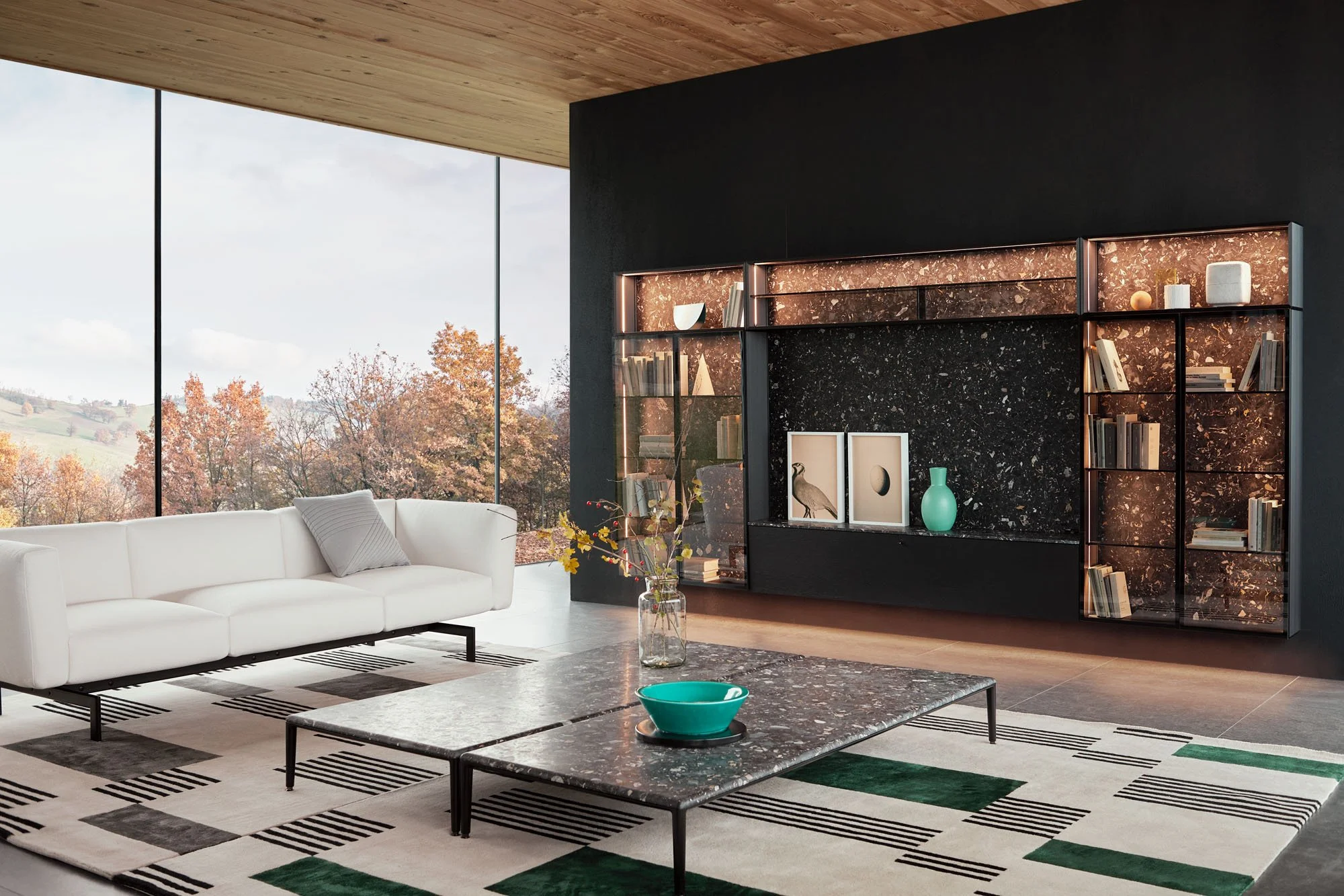 Modernes Wohnzimmer mit großen Fenstern, weißen Sofa, schwarzen Marmortisch, modernen dekorativen Gegenständen und einem Bücherregal vor einer schwarzen Wand, Blick auf eine herbstliche Landschaft.