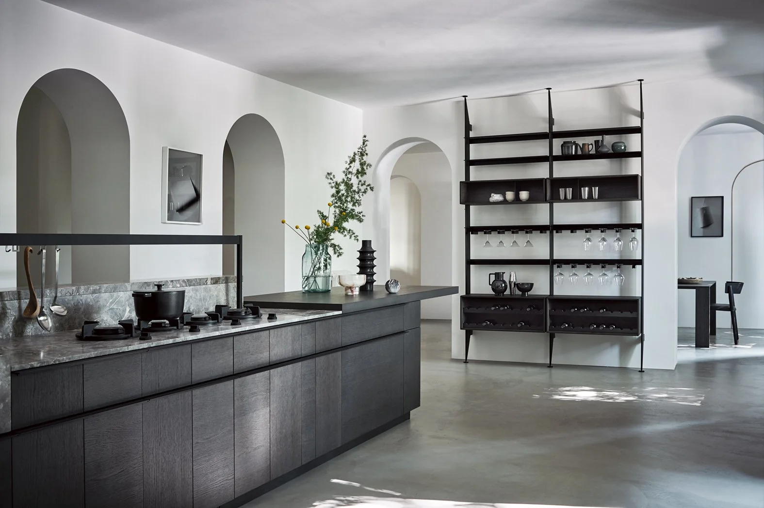 Moderne Küche mit schwarzen Unterschränken, Gasherd auf Marmor-Arbeitsplatte, Vasen und Dekorationsgegenständen auf dem Tisch, schwarze offene Regale mit Geschirr und Weinflaschen, weiße Wände mit Bögen.