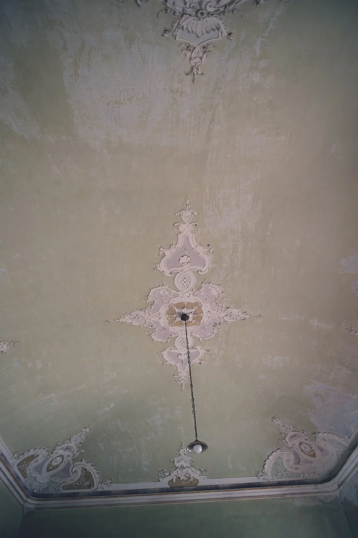 Decke mit vergoldeten und weißen Stuckornamenten in einem alten Gebäude.