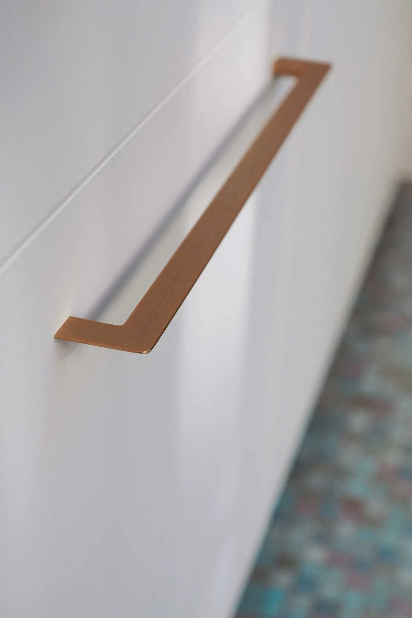 Nahaufnahme eines silbernen Handlaufes an einer weißen Wand, leicht unscharf im Hintergrund.