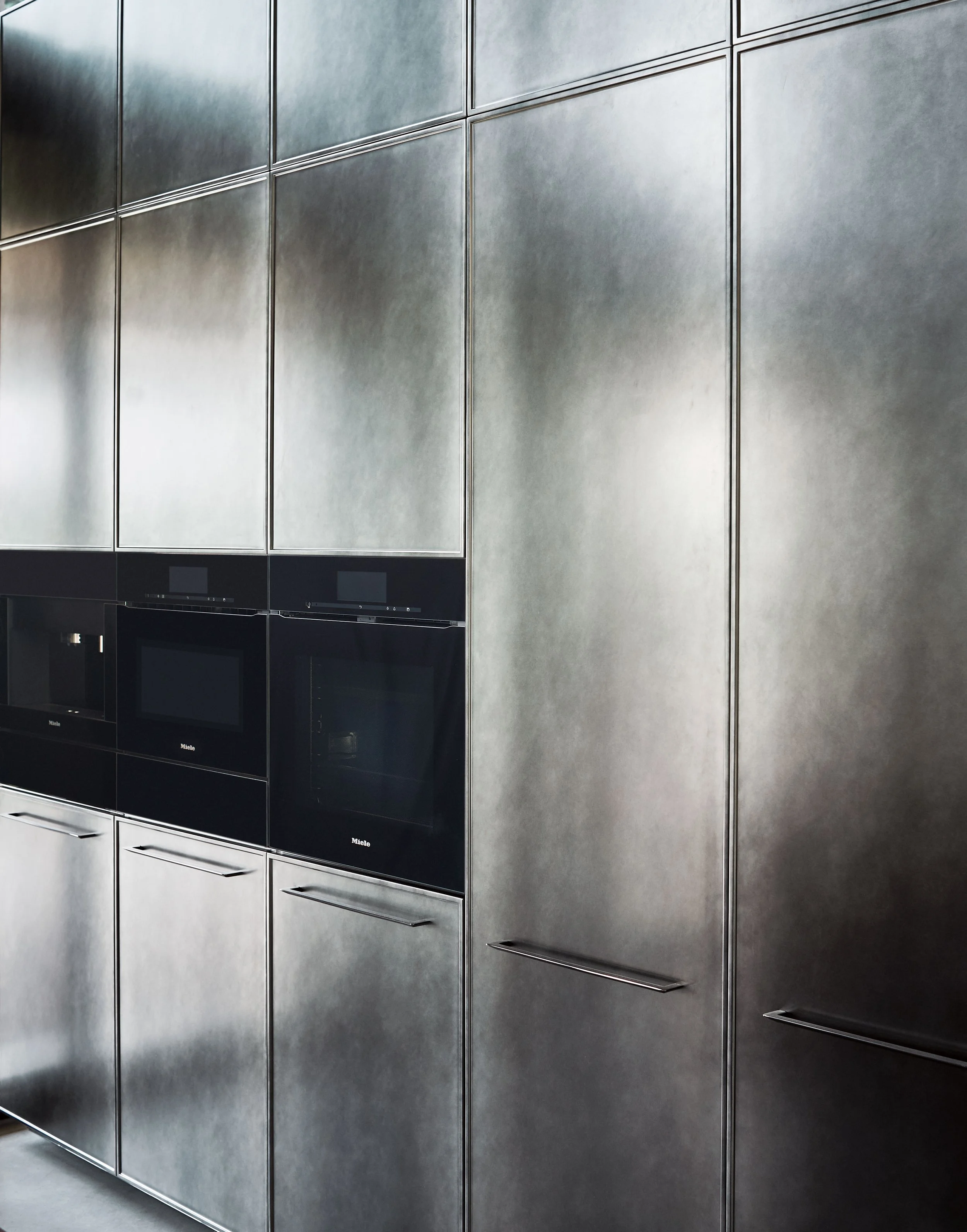 Eine Wand aus metallischen Türmen und Schubladen mit schwarzen Ofen- oder Mikrowellen-Geräten darunter.
