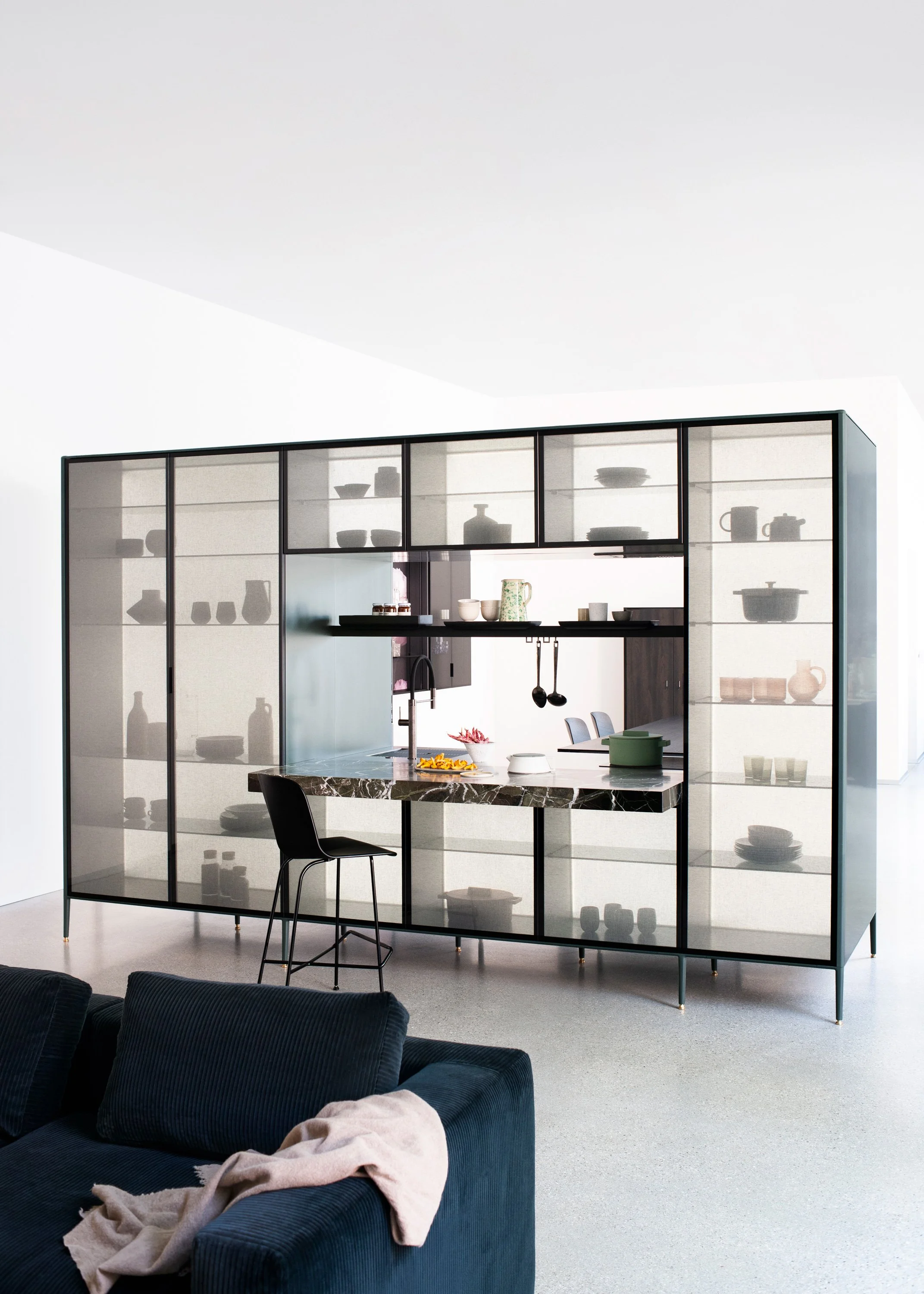 Moderner Raum mit schwarzem glaskabinet und schwarzem stuhl, sofa mit decke im Vordergrund.