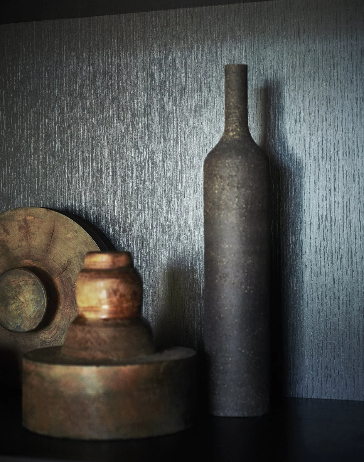 Drei antike, metallene Gegenstände in unterschiedlichen Formen, vor einer dunkelgrauen, geriffelten Wand.