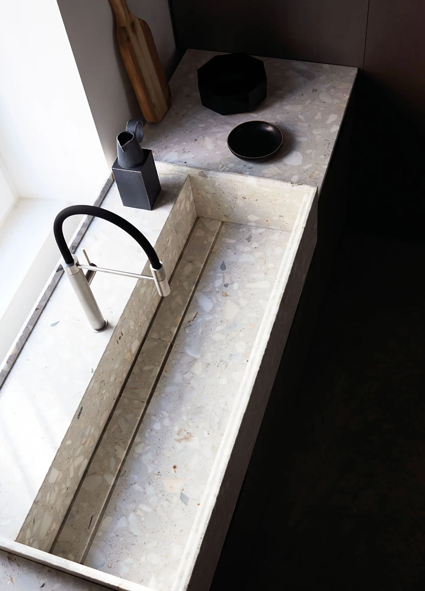 A modern kitchen sink with a black faucet and a beige marble countertop, decorated with black and wooden bowls and decorative objects.