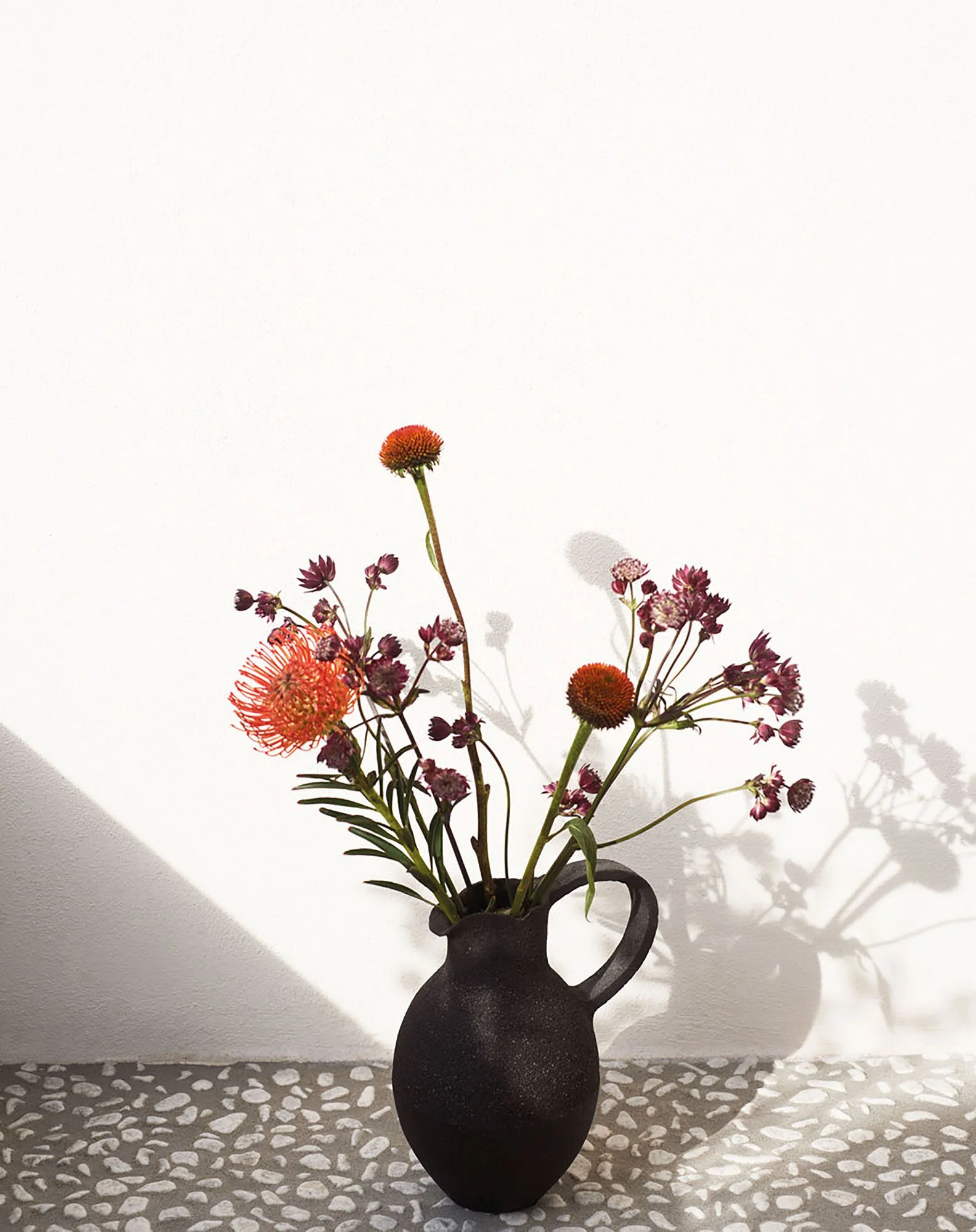 Schwarze Vase mit bunten Blumen, auf grauem Musterteppich, Hintergrund weiß