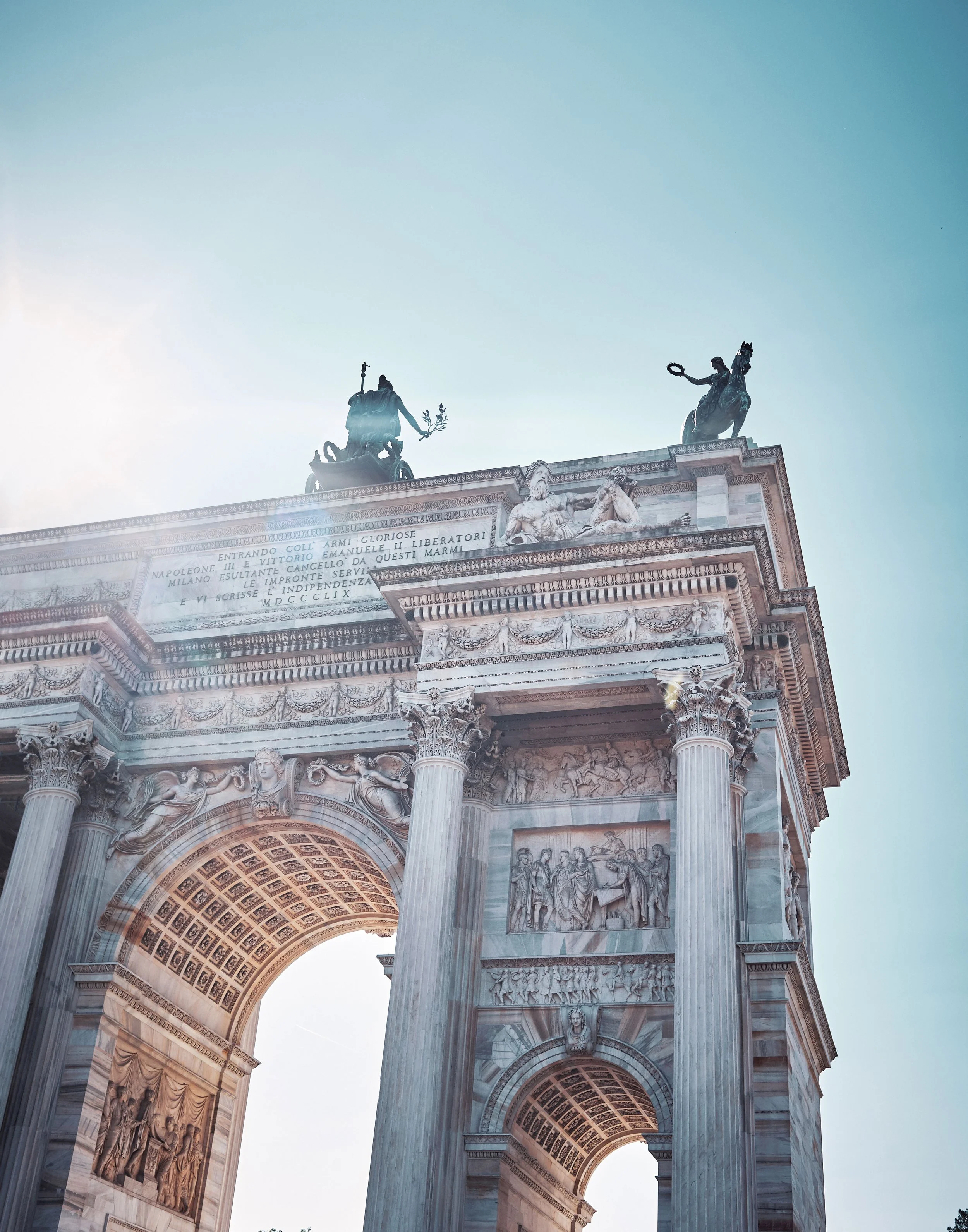 Blick auf den Arc de Triomphe in Paris, Frankreich, mit Statuen und architektonischen Verzierungen an der Spitze des Denkmals, gegen den blauen Himmel.