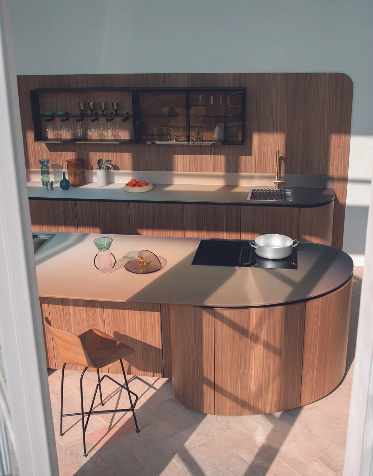 Moderne Küche mit Holzfronten, weißen Arbeitsflächen, Geschirr, Gläsern und Küchenutensilien, Sonnenschatten auf dem Boden.