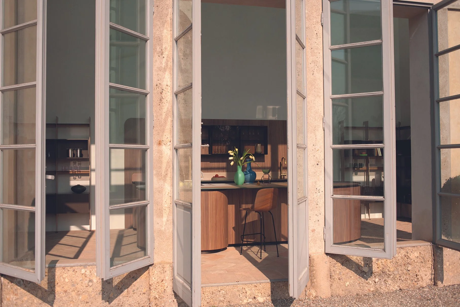 Offene französische Fenster mit Blick in eine moderne Küchenzeile, auf der eine grüne Vase mit weißen Tulpen steht.
