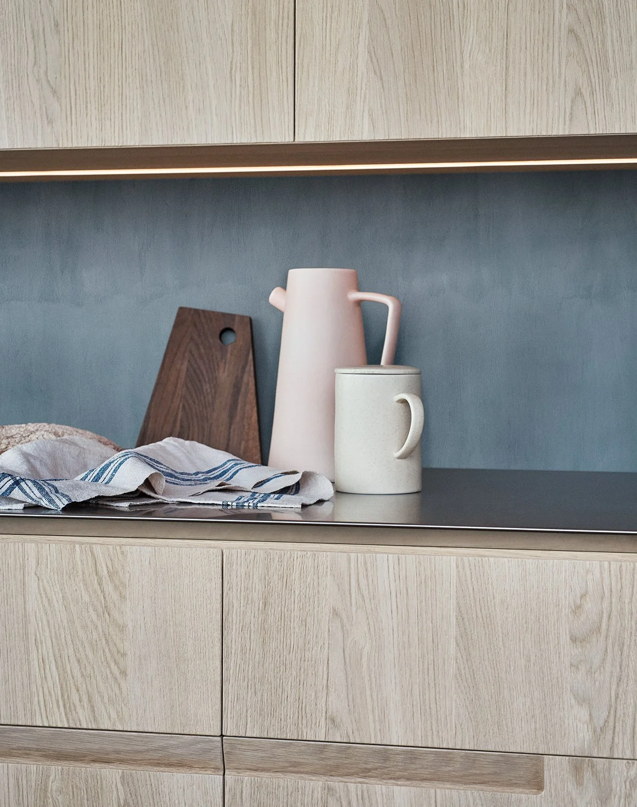 Küchennahe Aufbewahrung mit Teekannen, Bechern und einem Holzbrett auf einer schwarzen Oberfläche, mit Holzschränken im Hintergrund.