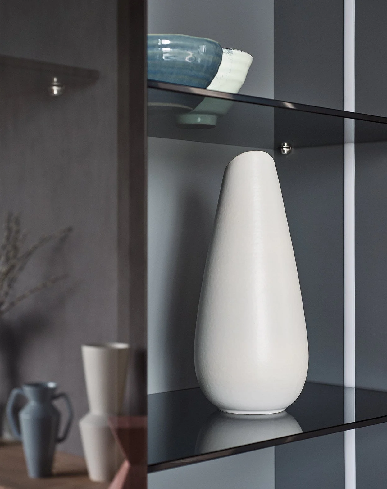 Ein großer, weißer, geschwungener Keramikvase auf einer schwarzen Glasregal in einem modernen, minimalistischen Raum.
