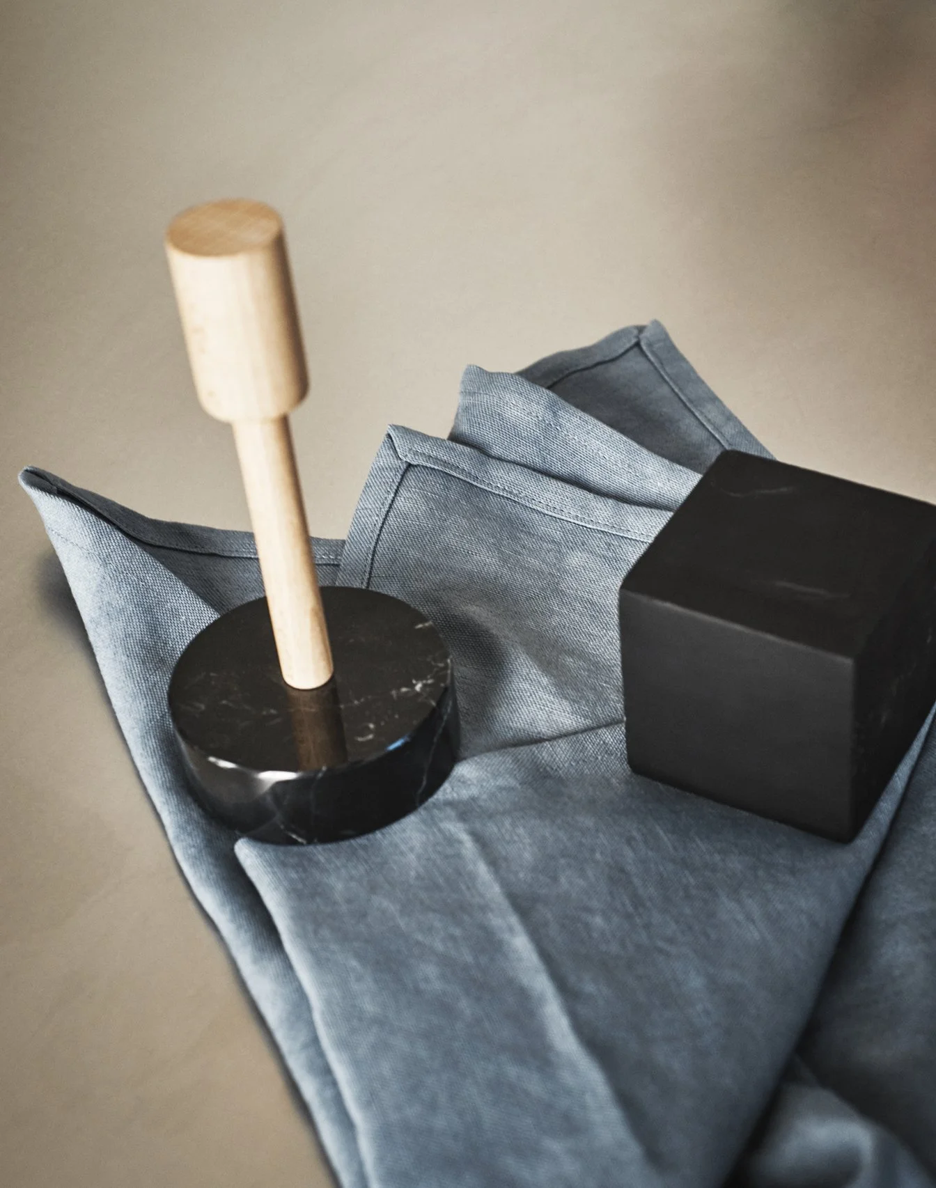 Minimalistisches Stillleben mit einem schwarzen Kerzenhalter, einem grauen Tuch, einer eleganten schwarzen Schachtel und einer schwarzen Kugel, arrangiert auf einem dunkelgrauen Tisch. Die reduzierte Farbpalette und die klaren Formen erzeugen eine mo