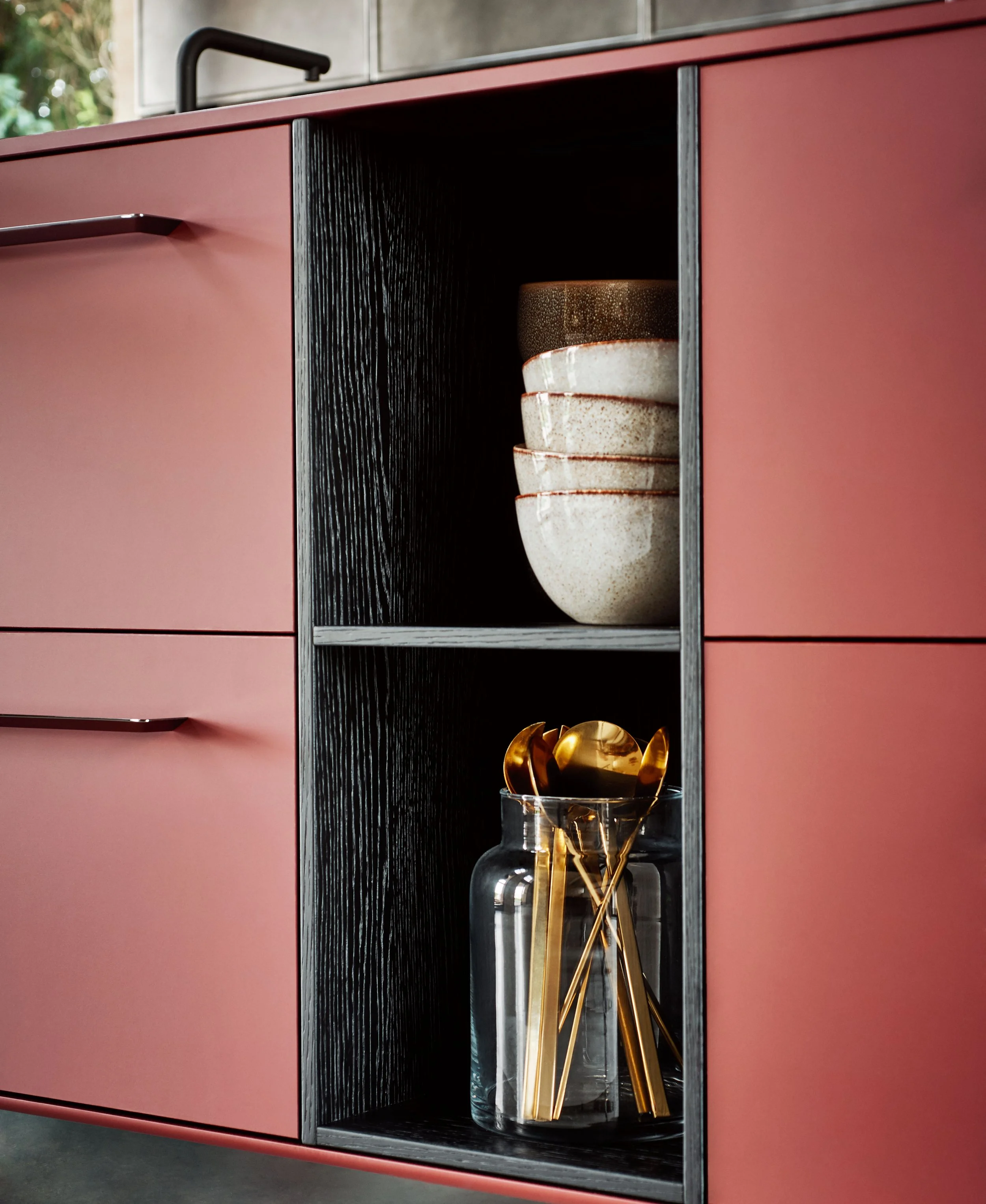 Ein roter Schrank mit schwarz geriffeltem Inneren. Darin befinden sich mehrere beige Keramikkörbe. Im Glasvase auf dem Boden steht ein goldener Dekorationsgegenstand mit mehreren gebogenen Formen.