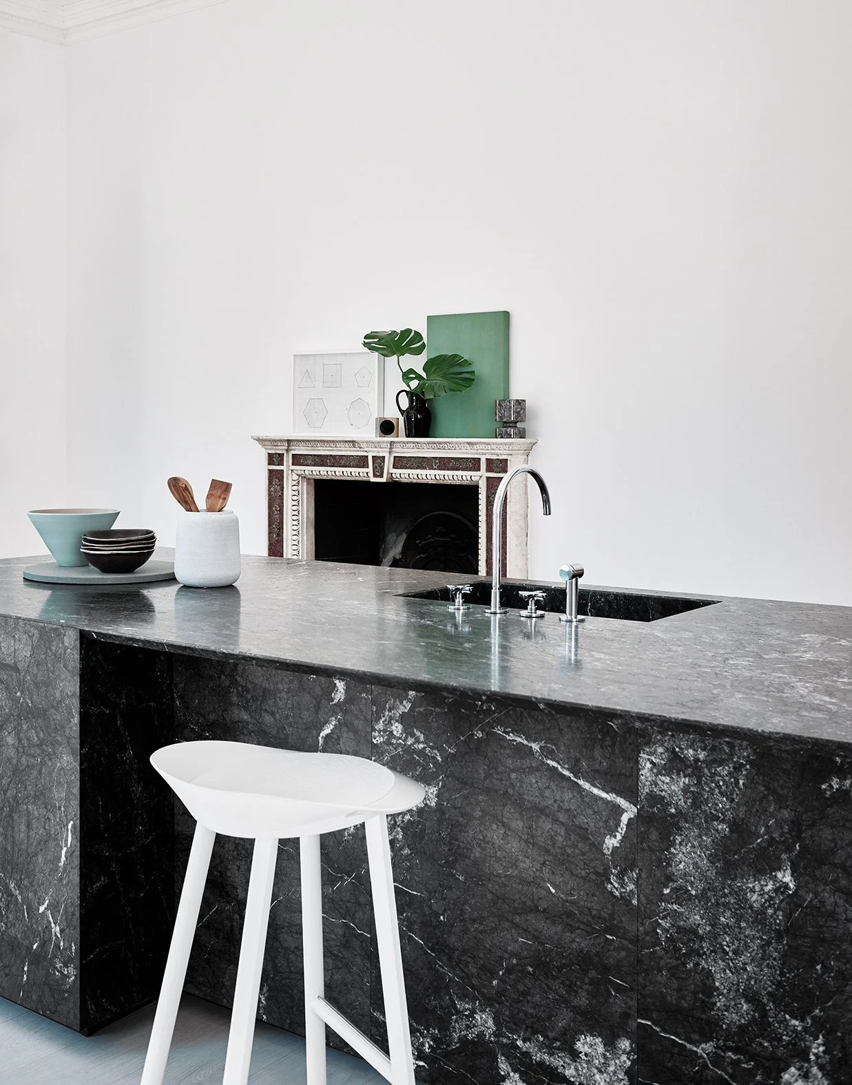 Moderne Küche mit schwarzer Marmor-Theke, weißen Stuhl, grünen Pflanzen und minimalistische Dekoration.