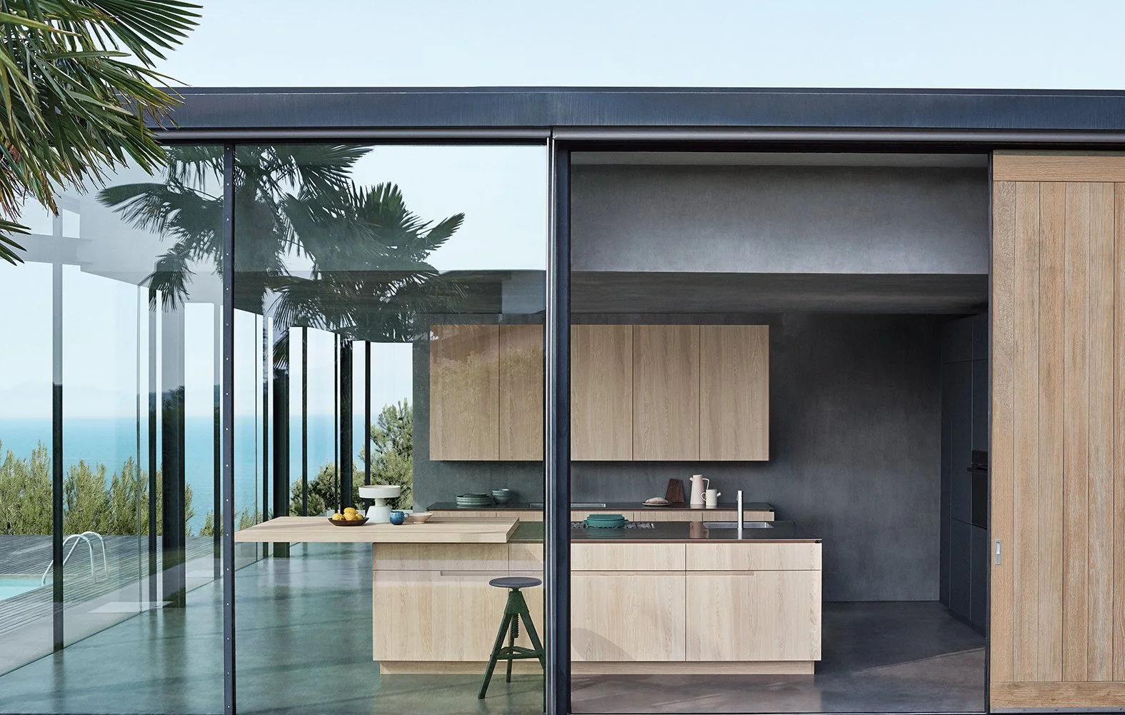 Moderne Küche mit Holzakzenten und großen Glaswänden, Blick auf den Garten und das Meer im Hintergrund.