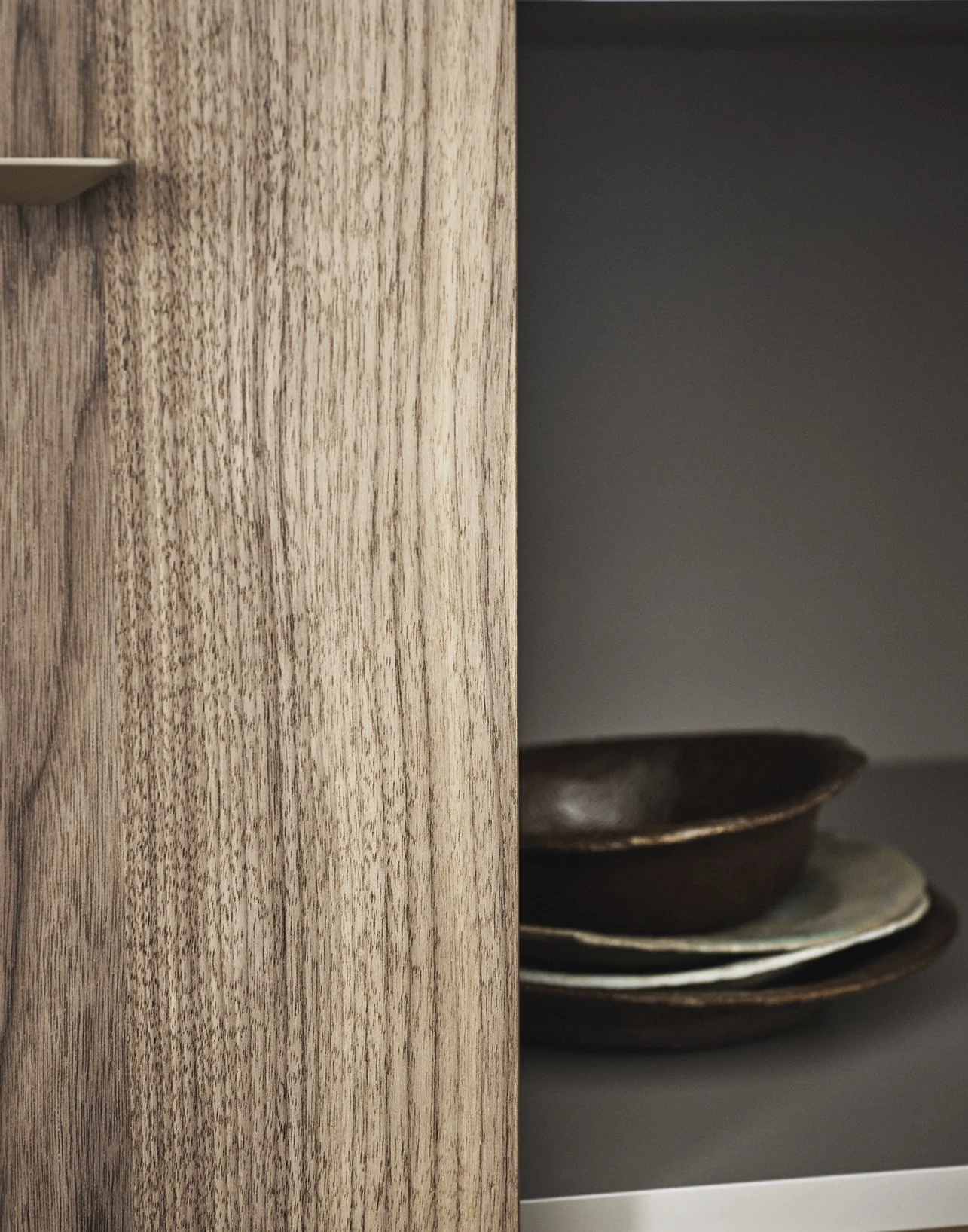Nahaufnahme von einem Holzregal mit mehreren dunklen Keramikschalen auf einem grauen Hintergrund.