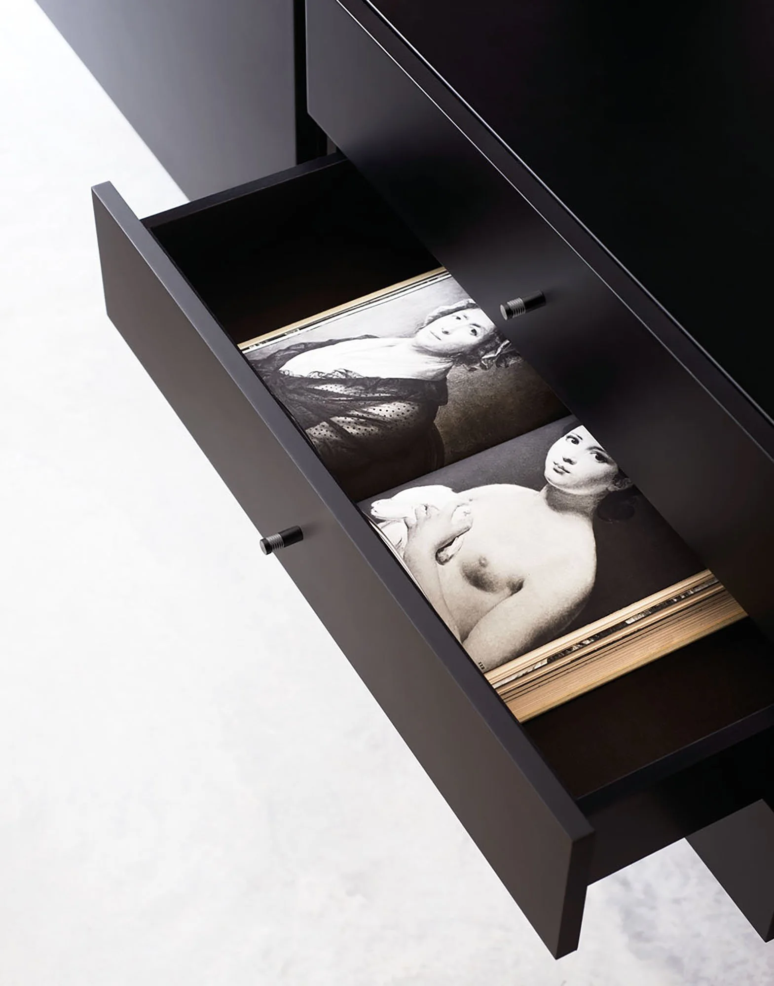 Offenes schwarzes Schrank mit Fotos von Frauen im Inneren, der auf einem weißen Boden steht.