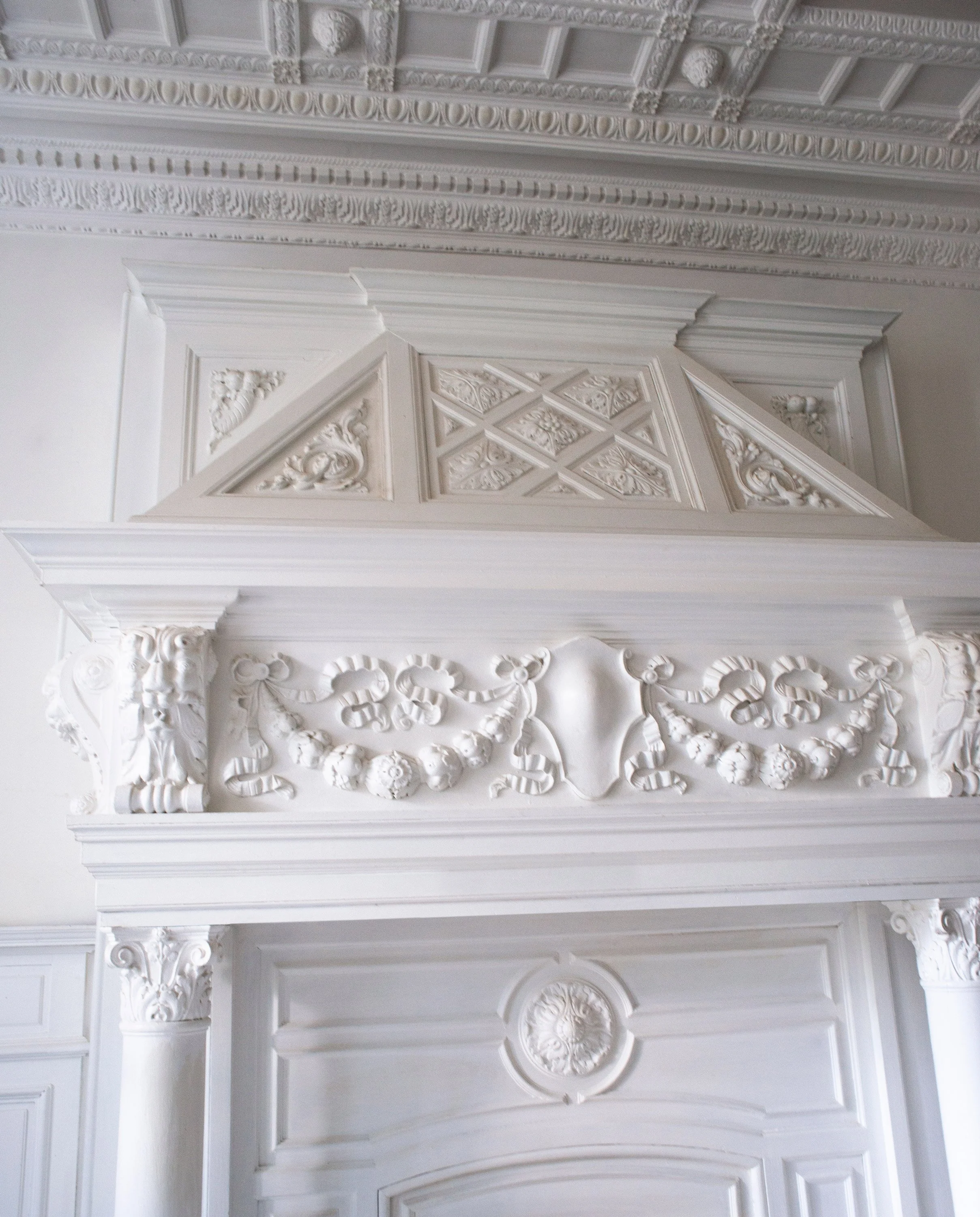 Weiße, kunstvoll verzierte Decke und Zierleisten mit floralen Mustern und klassischen Ornamenten in einem eleganten Raum.