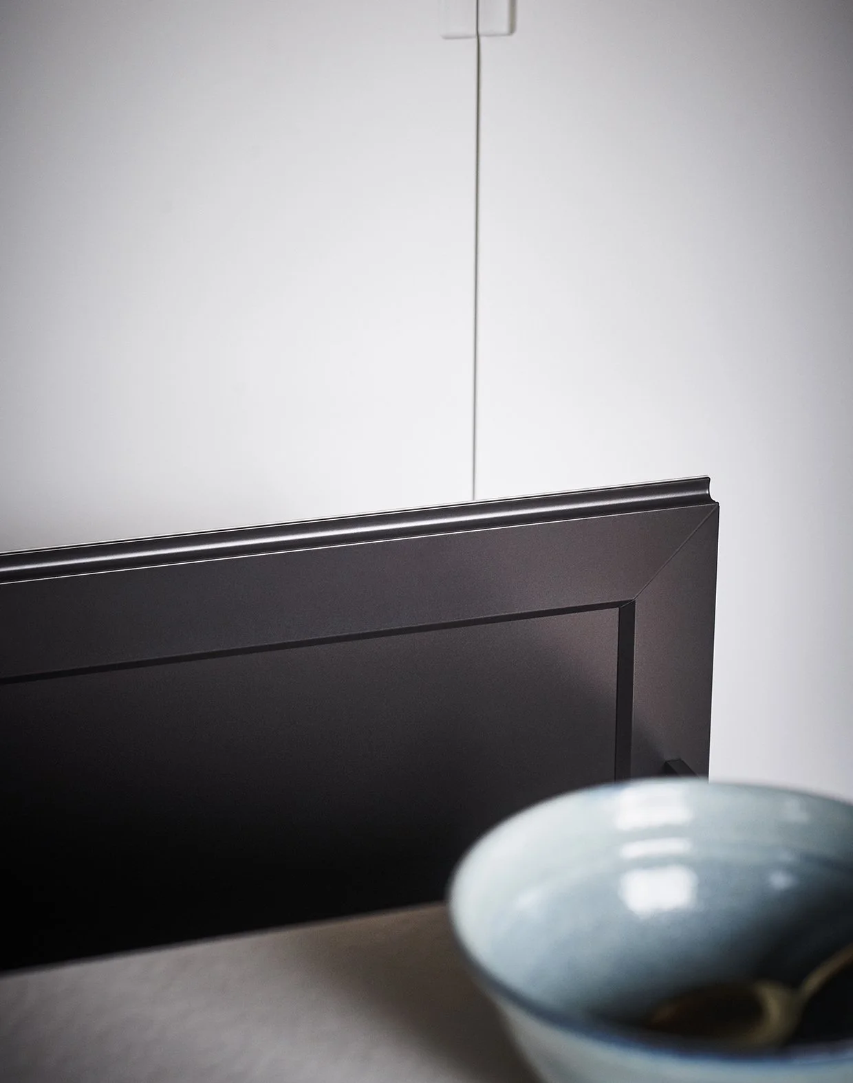Ein dunkler Fernseher auf einem Tisch, eine weiße Wand im Hintergrund, teilweise sichtbar eine weiße Schüssel am unteren rechten Bildrand.