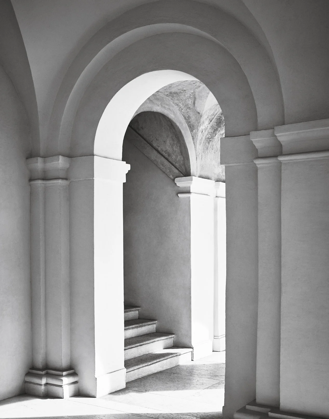 Ein weißer, mehrstöckiger Treppe in einem klassischen Gebäude mit weißen Wänden und Bögen.