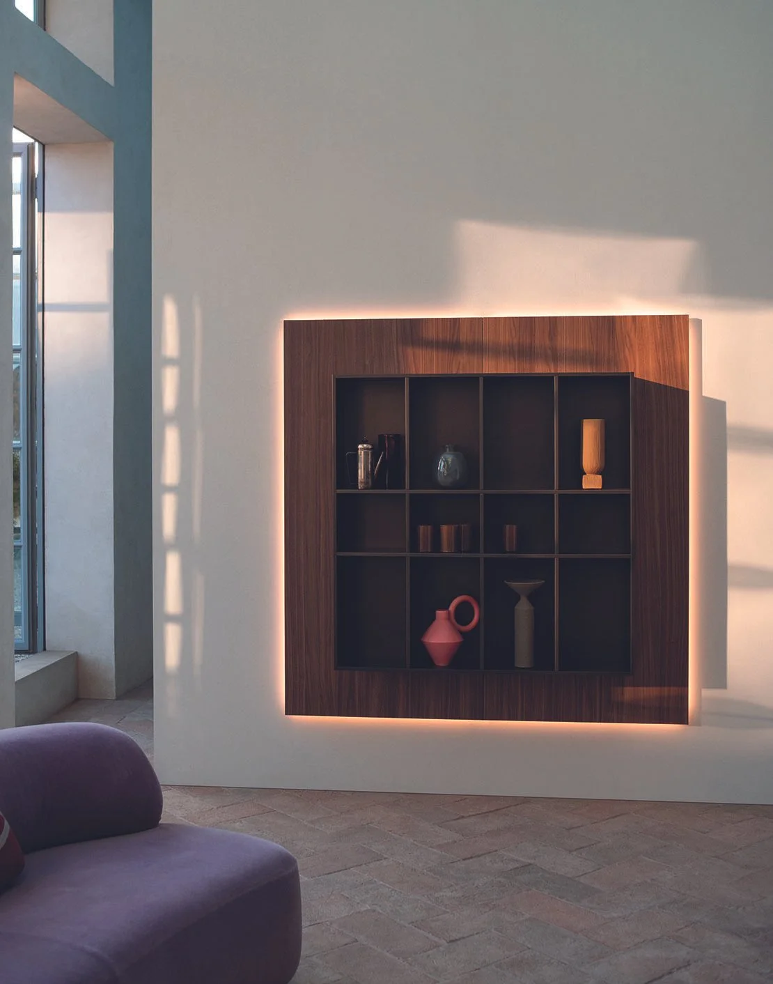 Moderne Wandgestaltung mit beleuchteten Holzkastenregal, Dekorationsutensilien wie Gläser und Vasen, Fenster mit Tageslicht in einem hellen Raum.