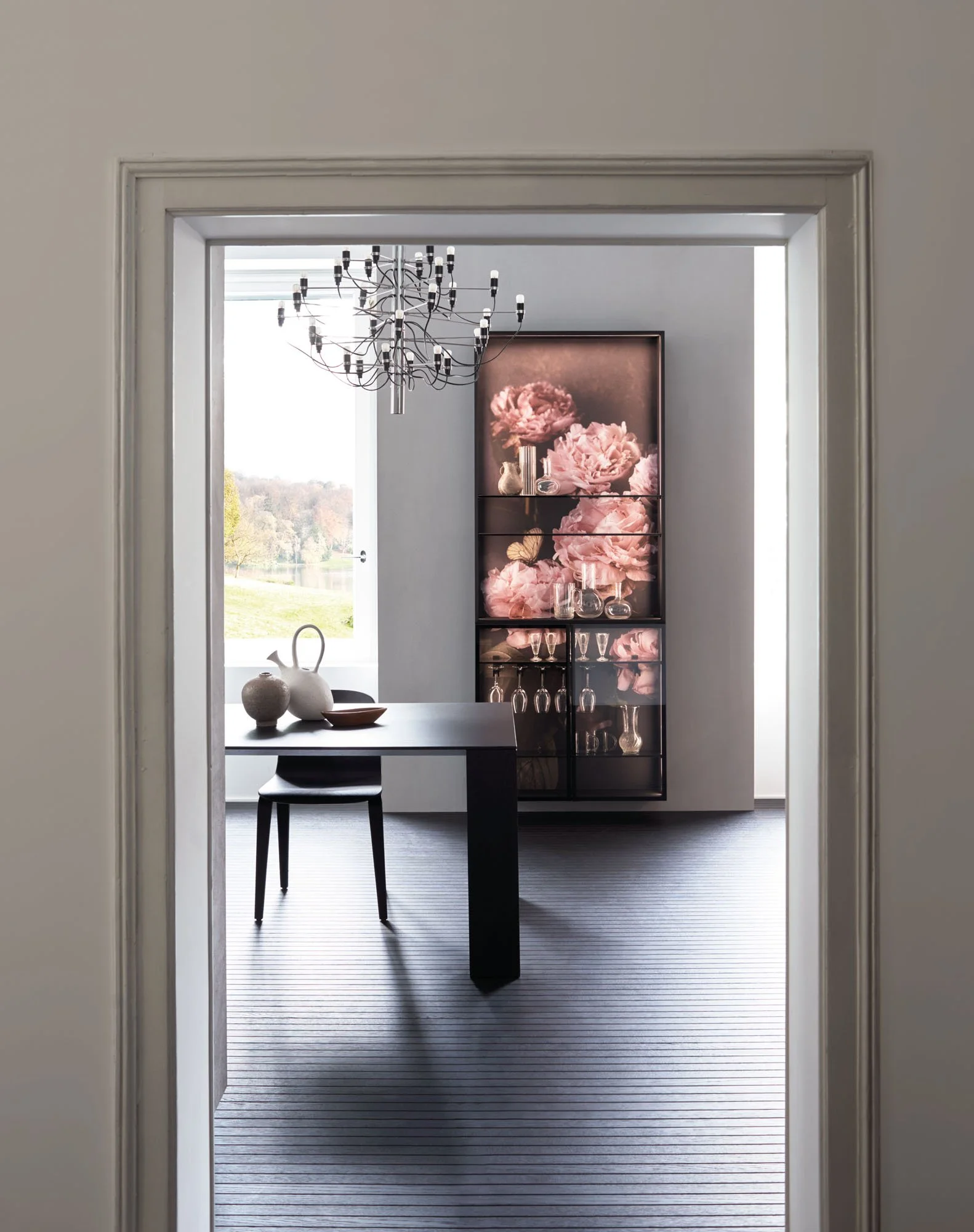 Ein Blick in einen modernen Essbereich mit einem schwarzen Esstisch, einer schwarzen Stuhllehne, einer großen Garderobe mit Blumenmotiv im Hintergrund und einem großen Fenster, das Tageslicht hereinlässt.