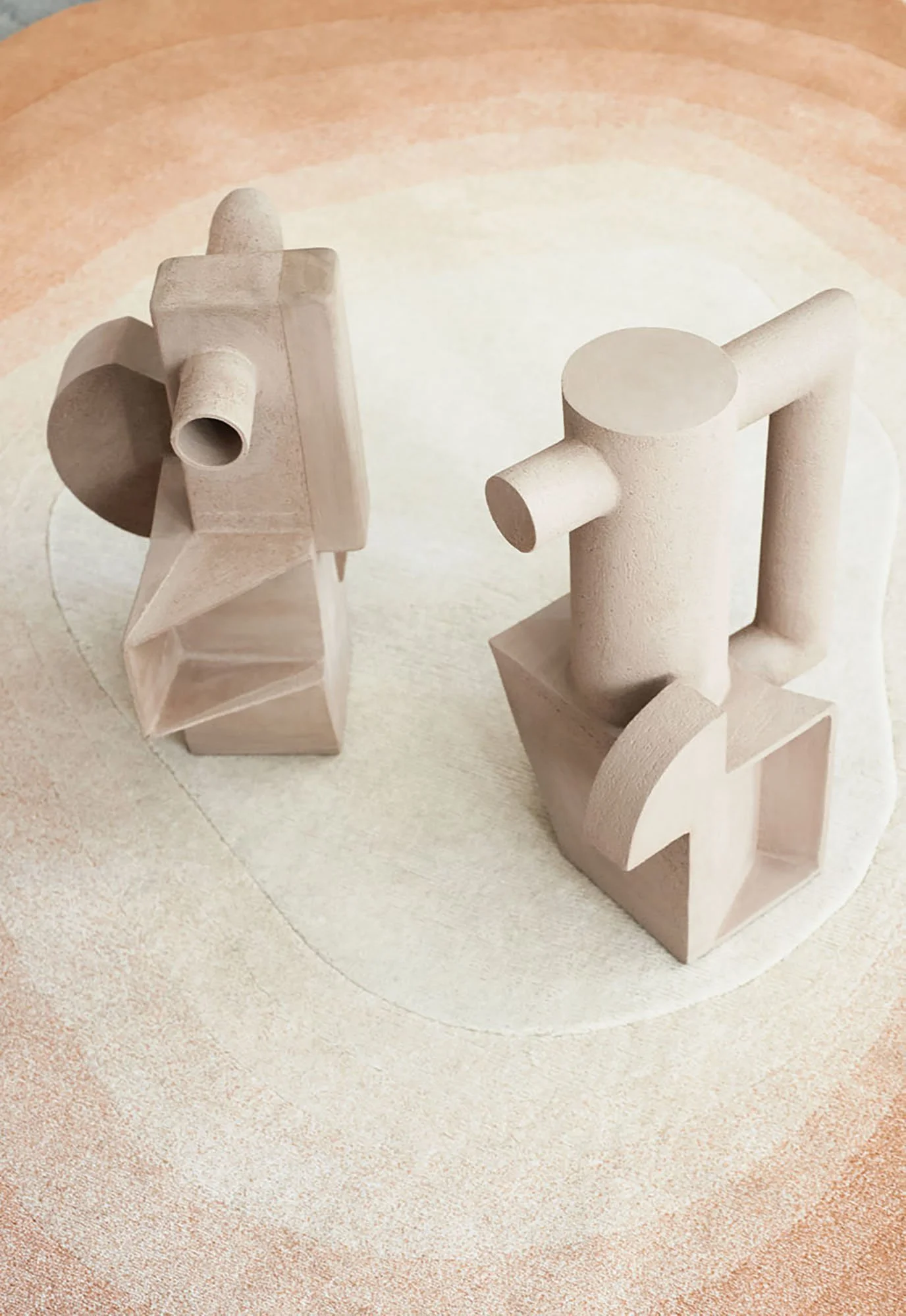 Zwei geometrische Skulpturen auf einem hellen, polierten Boden. Die Skulpturen sind aus hellem Holz oder Ton gefertigt und bestehen aus verschiedenen geometrischen Formen wie Würfeln, Zylindern und Kegeln.